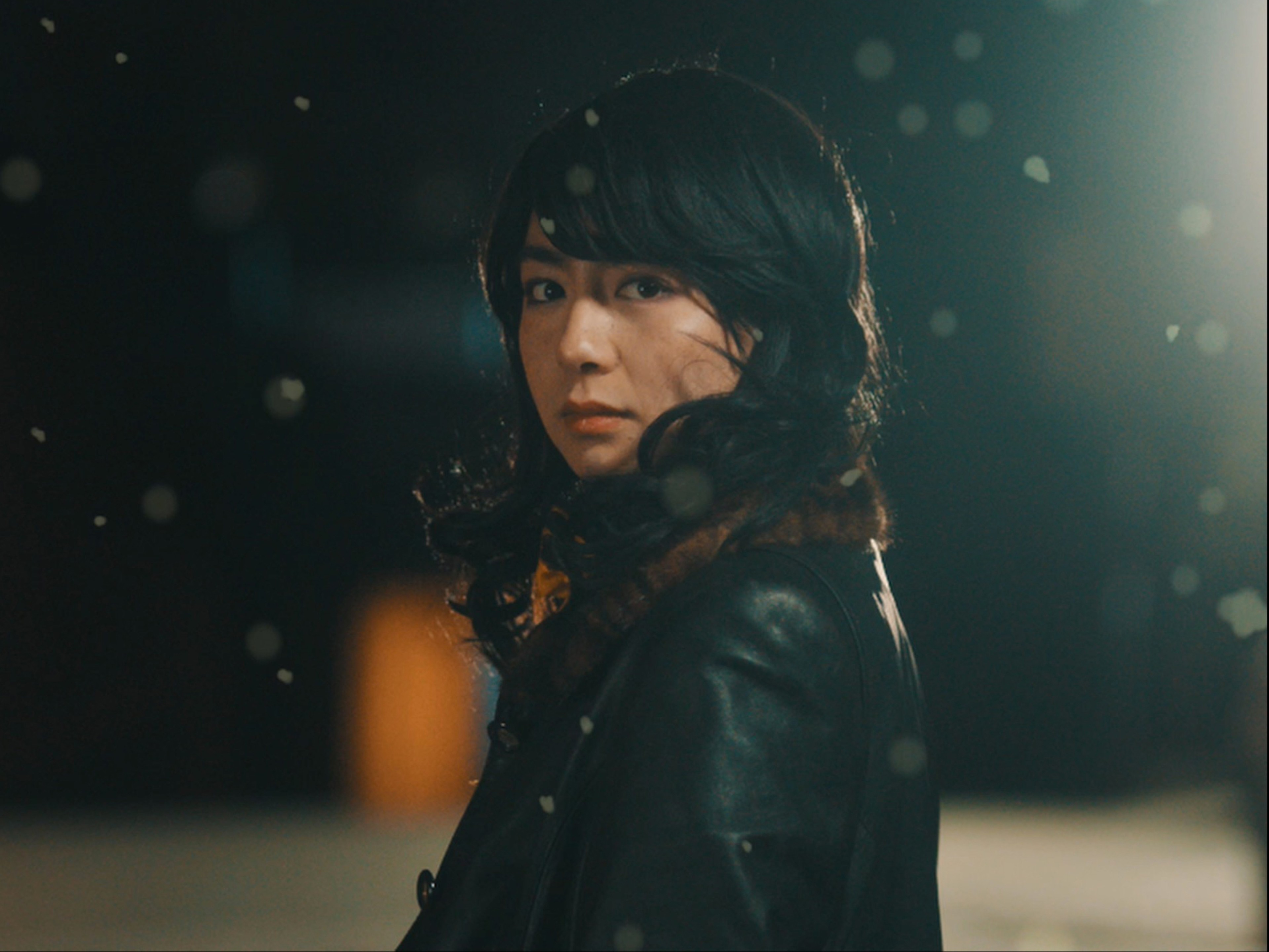 A woman looks into the camera surrounded by falling snow.