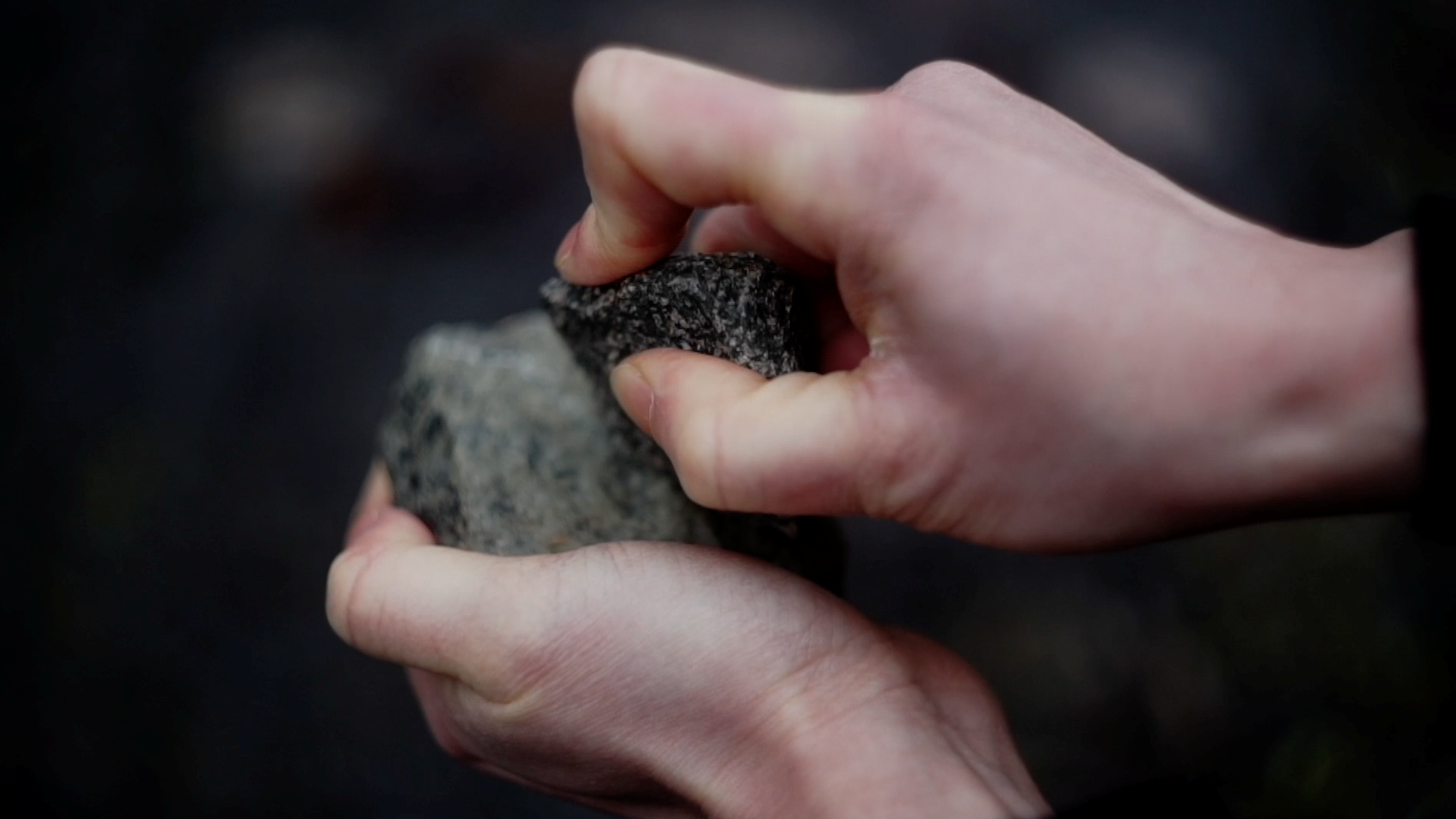 A pair of hands rubs two rocks against each other.