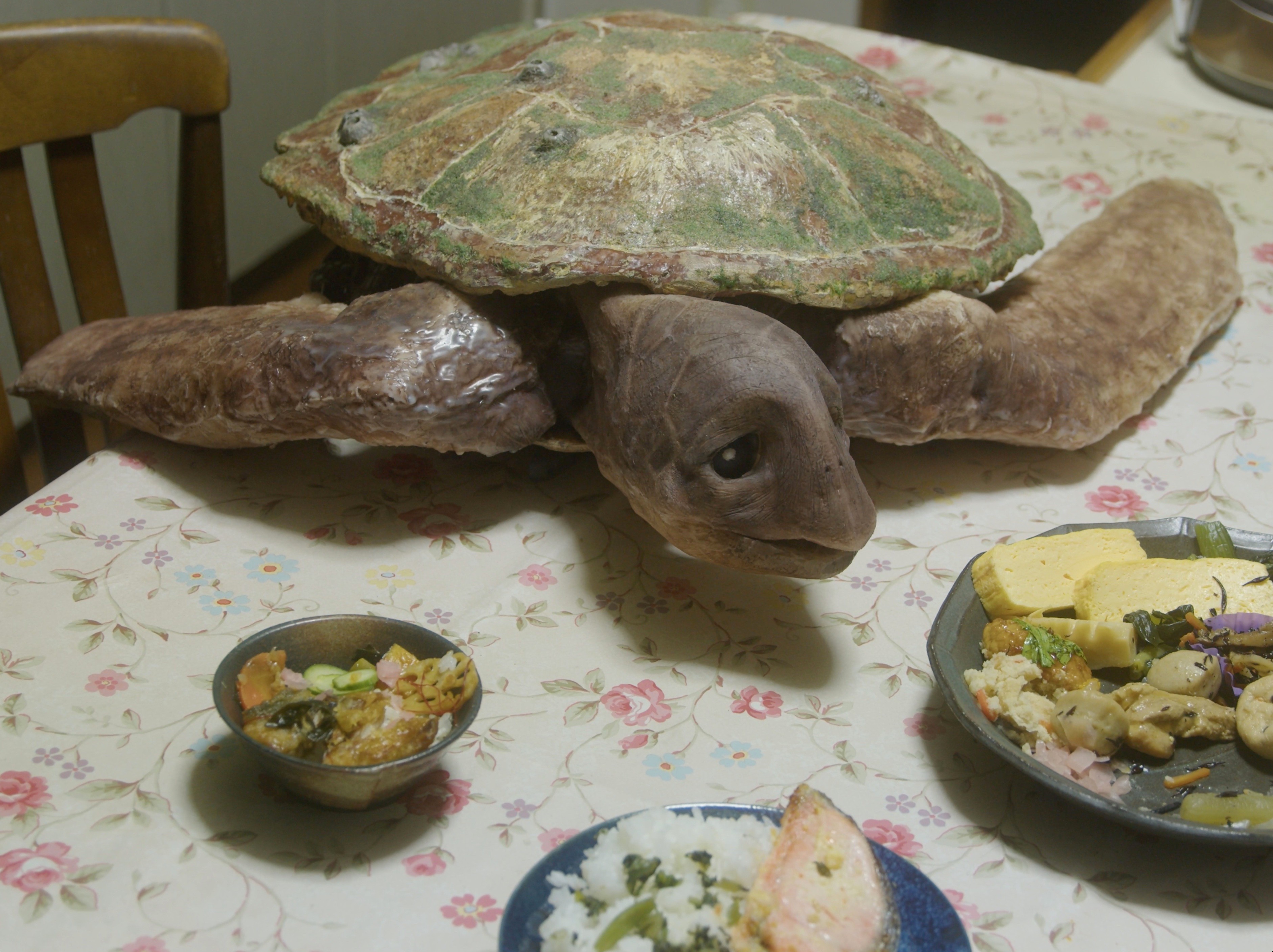 A large turtle sculpture rests on a dining table among plates and bowls of food.