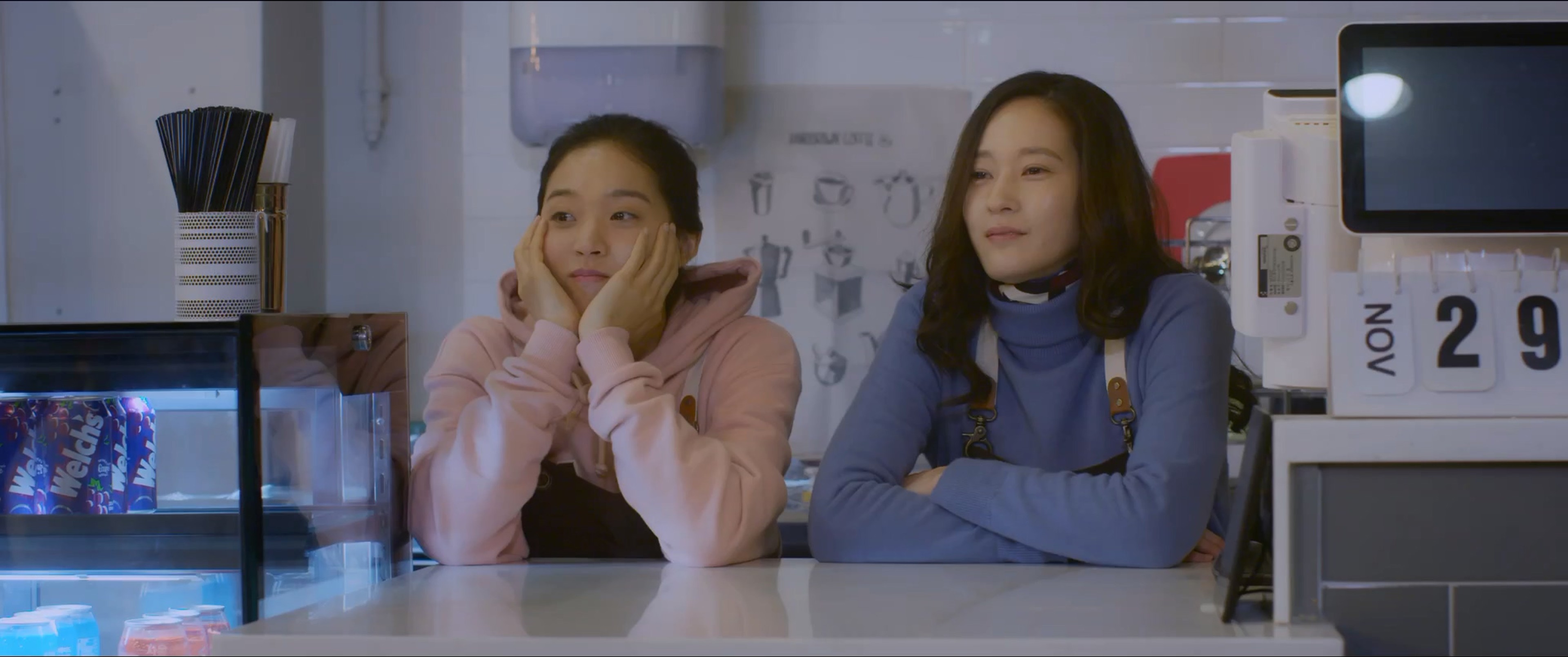 Two women sit side by side behind a cafe counter.