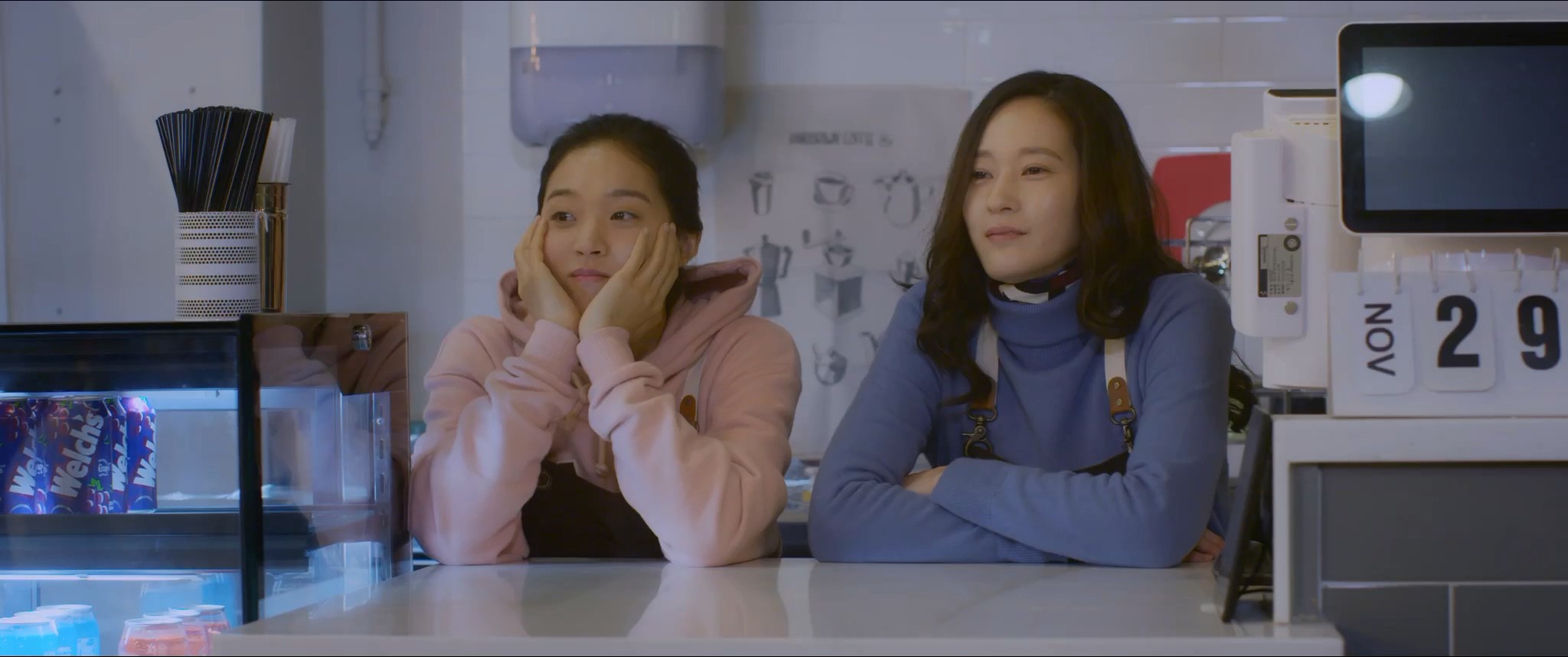 Two women sit side by side behind a cafe counter.