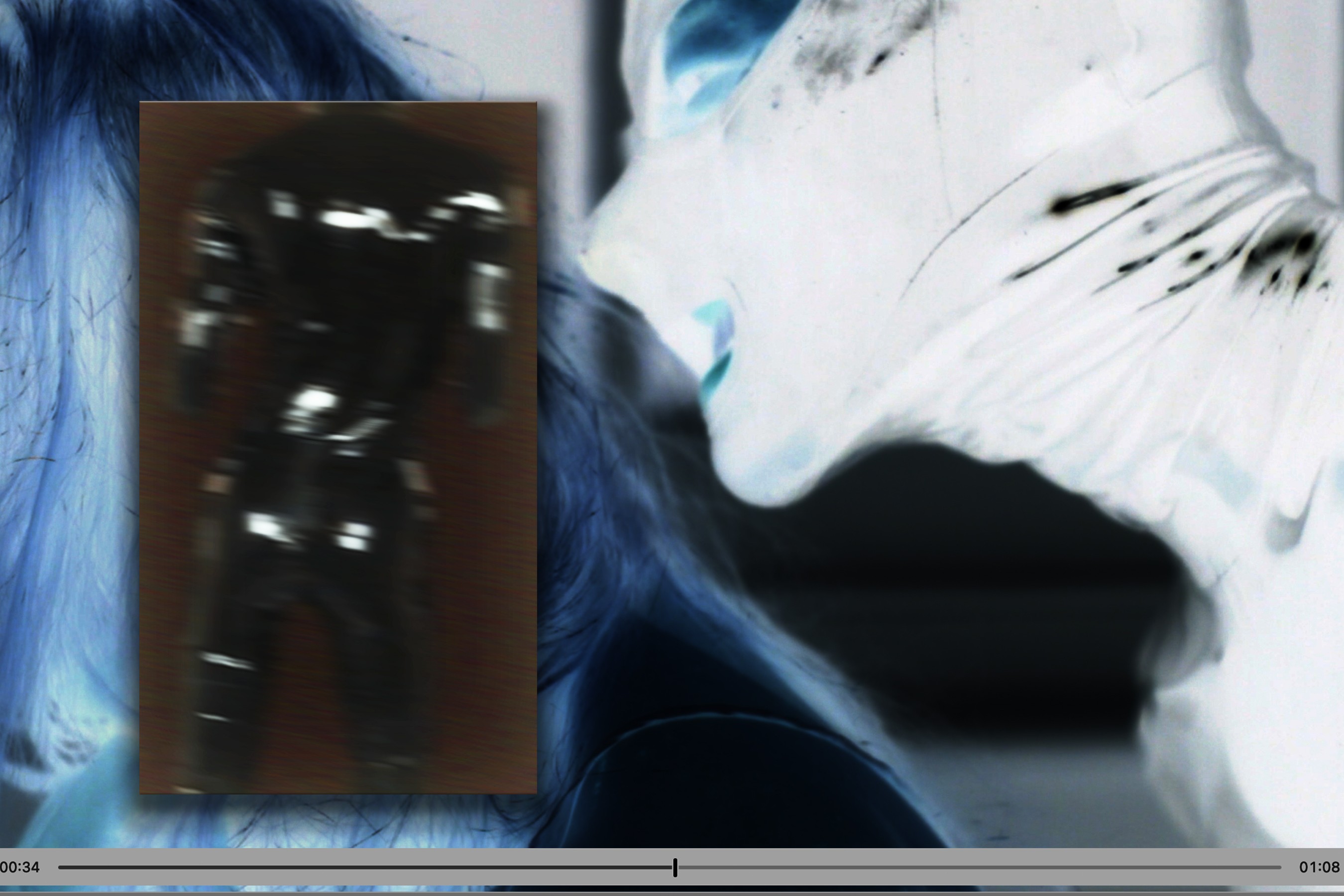 An abstract, inverted close-up of a face layered with a smaller dark rectangular image, shown within a video playback frame.