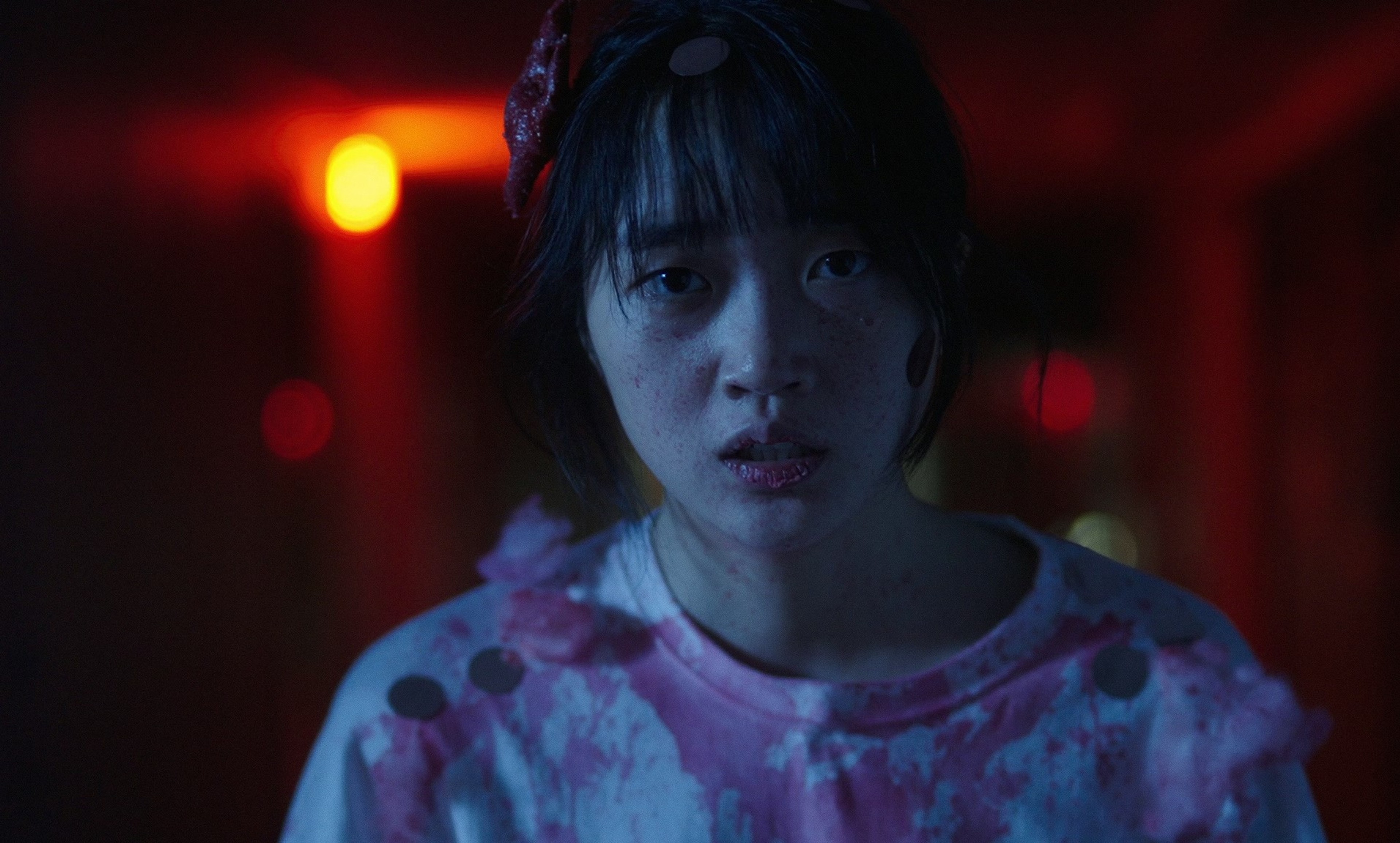 A young person in a pink costume looking directly ahead under red and blue lighting.
