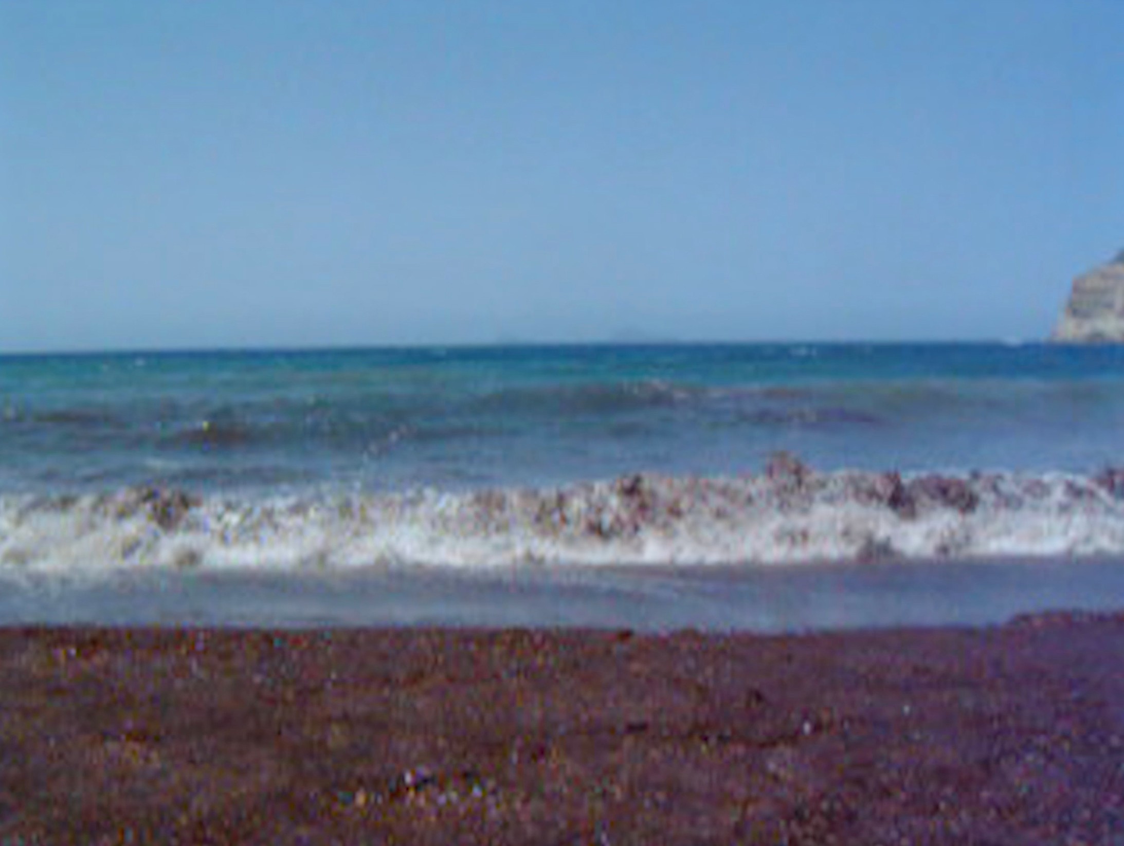 Waves breaking onto a dark shoreline beneath a clear blue sky.