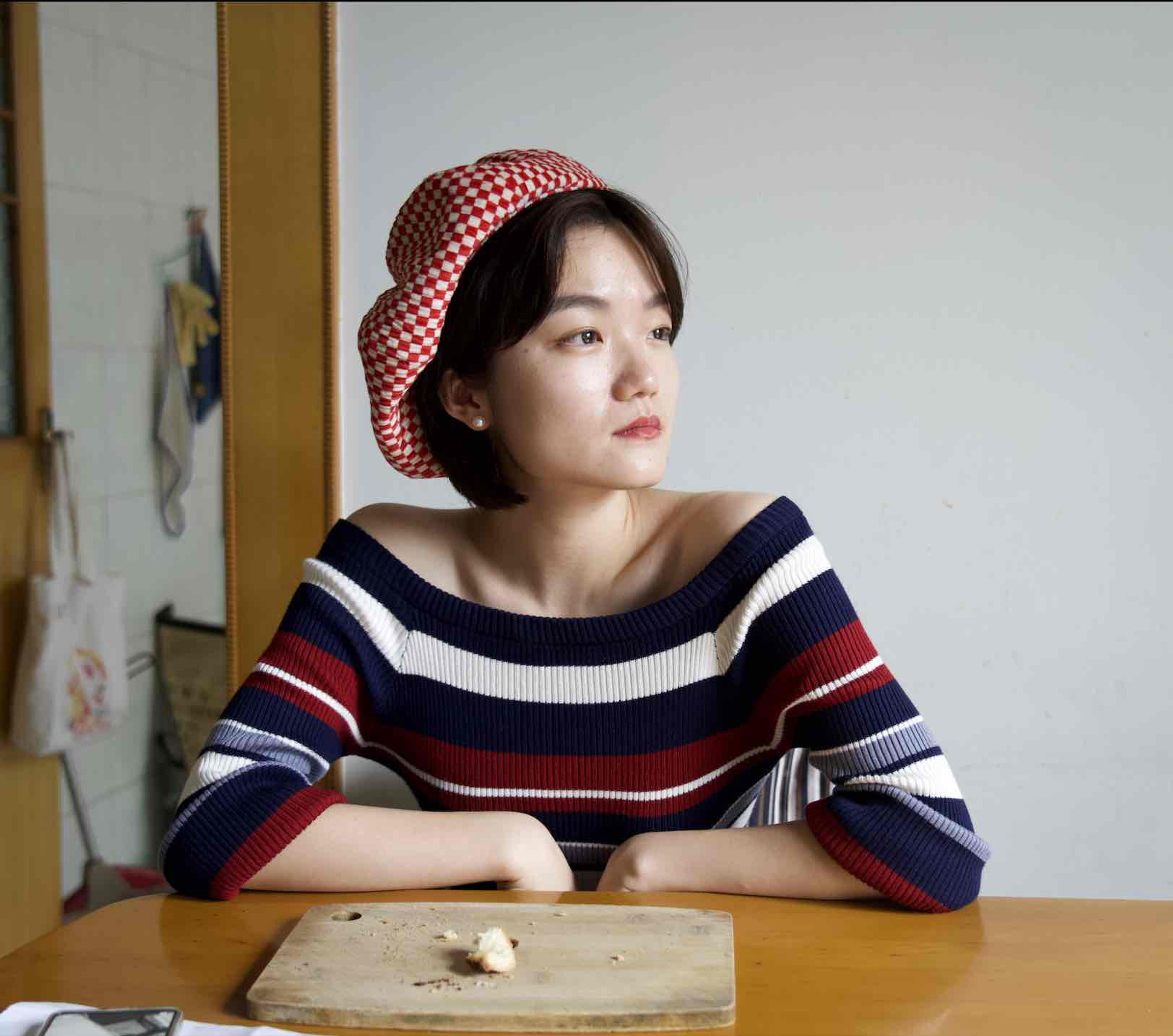 A woman wearing a red patterned headscarf and striped top sitting at a table and looking to the side.
