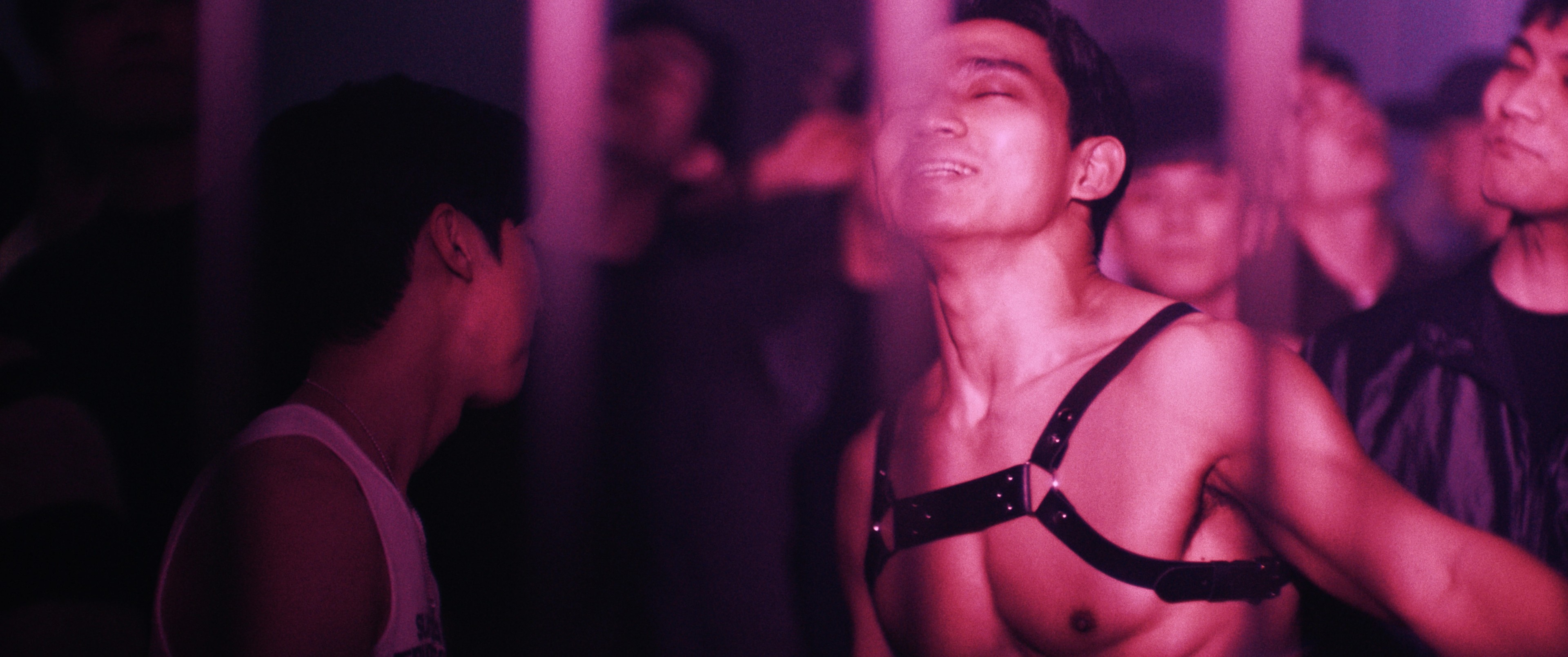 A man wearing a harness dances in a gay club.