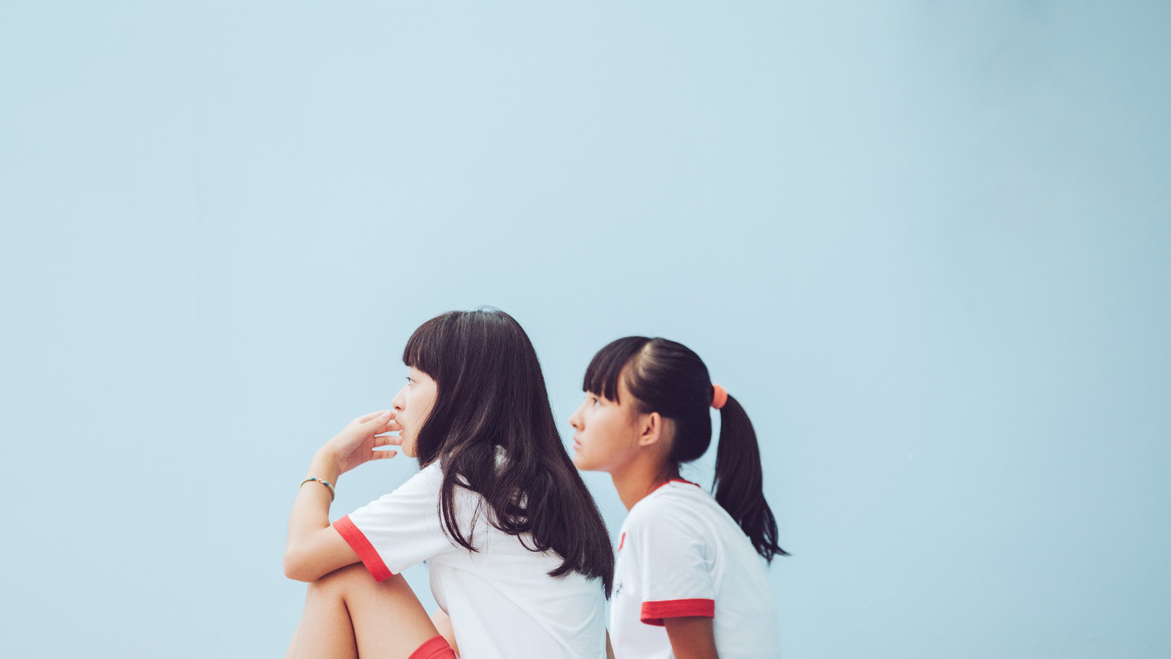Two young girls sit against a light blue background.