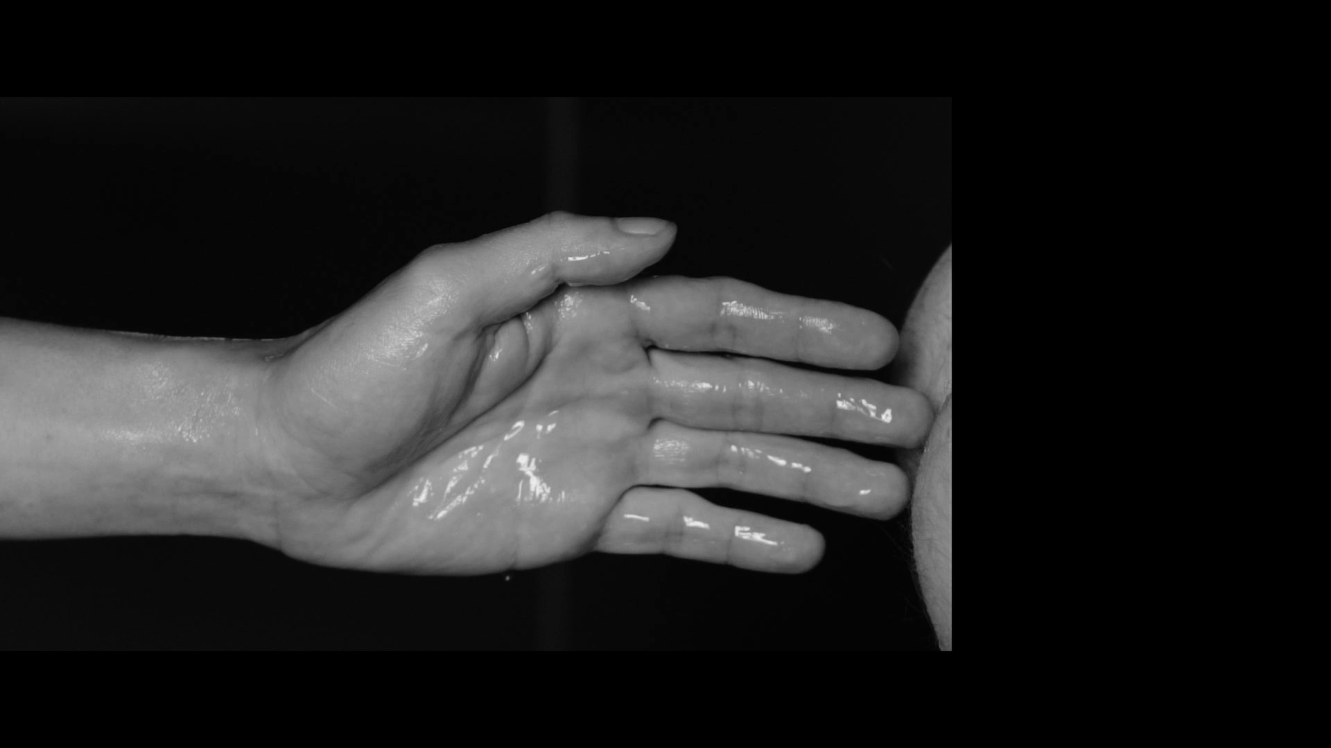 A black-and-white close-up of two wet hands reaching toward each other against a dark background.