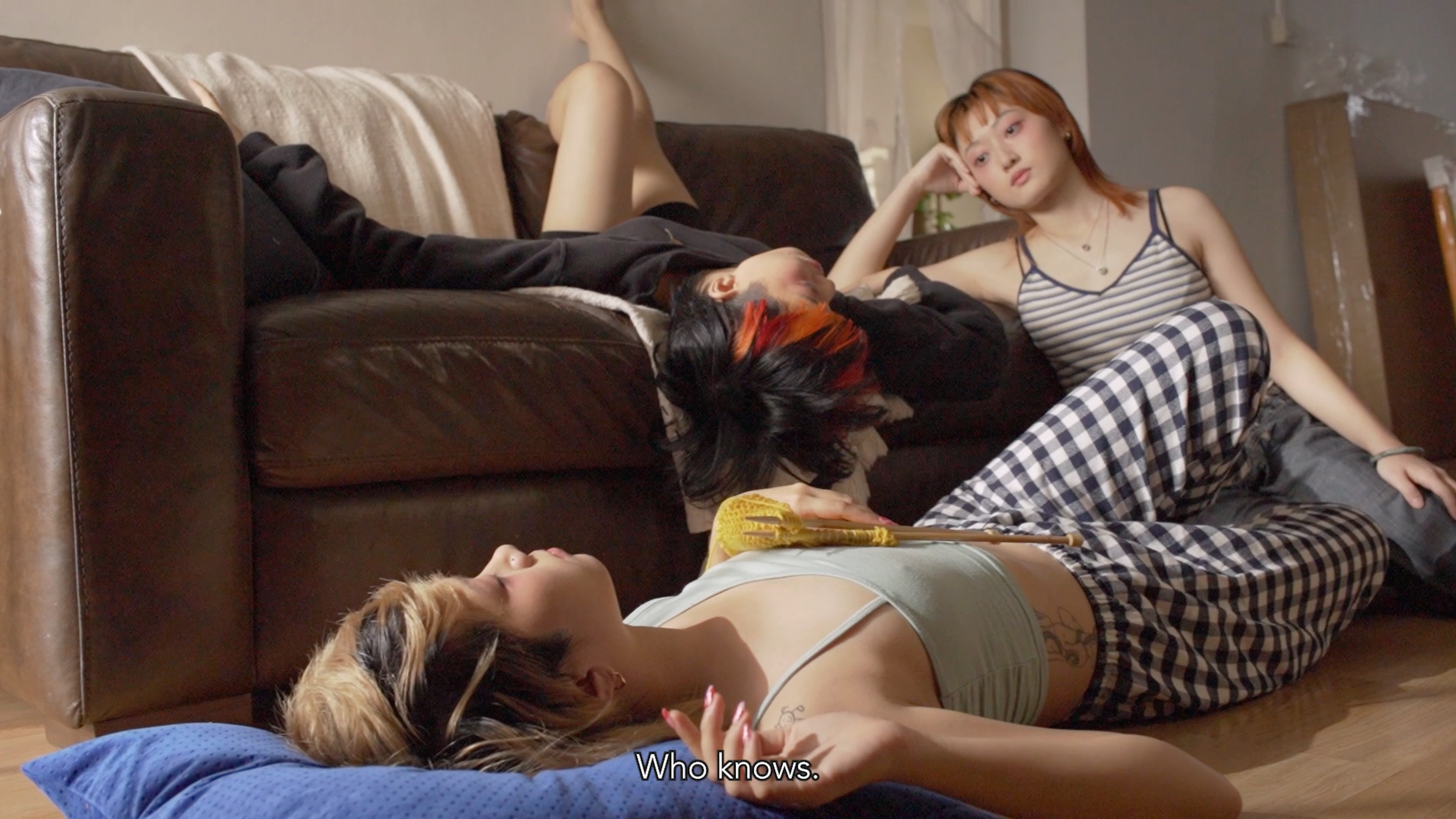 Three people lounging together on and beside a sofa in a sunlit living room.