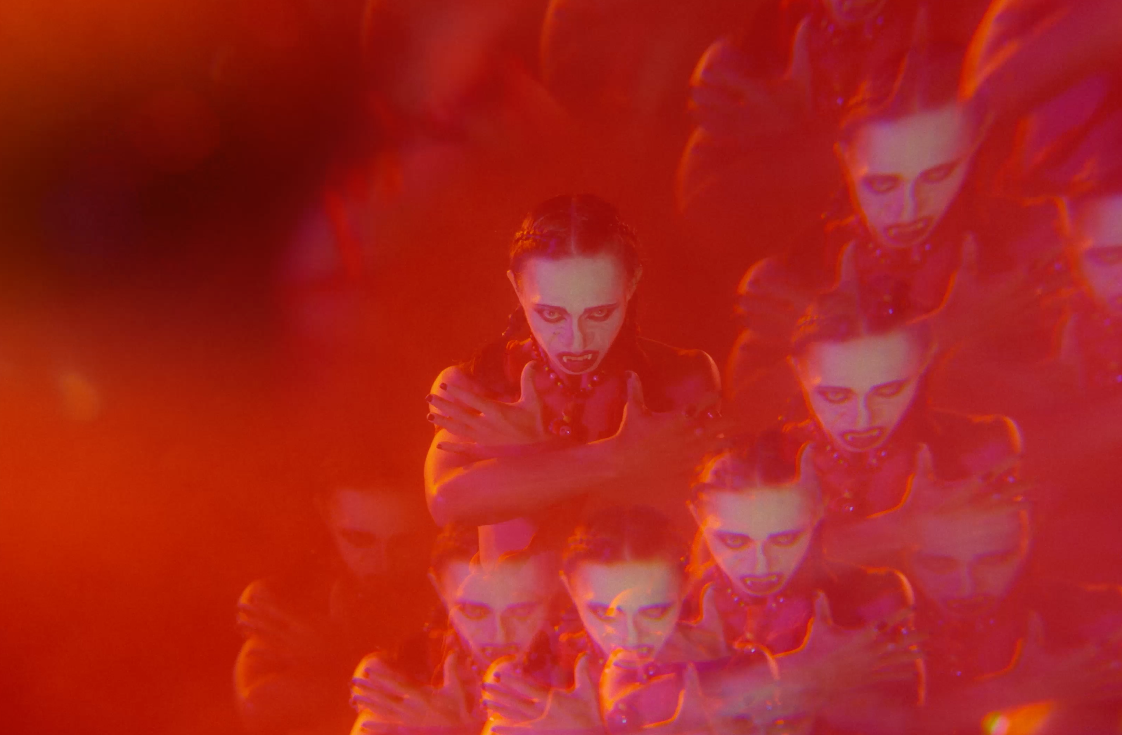 Multiple overlapping images of a performer with dramatic makeup, bathed in intense red and purple light.