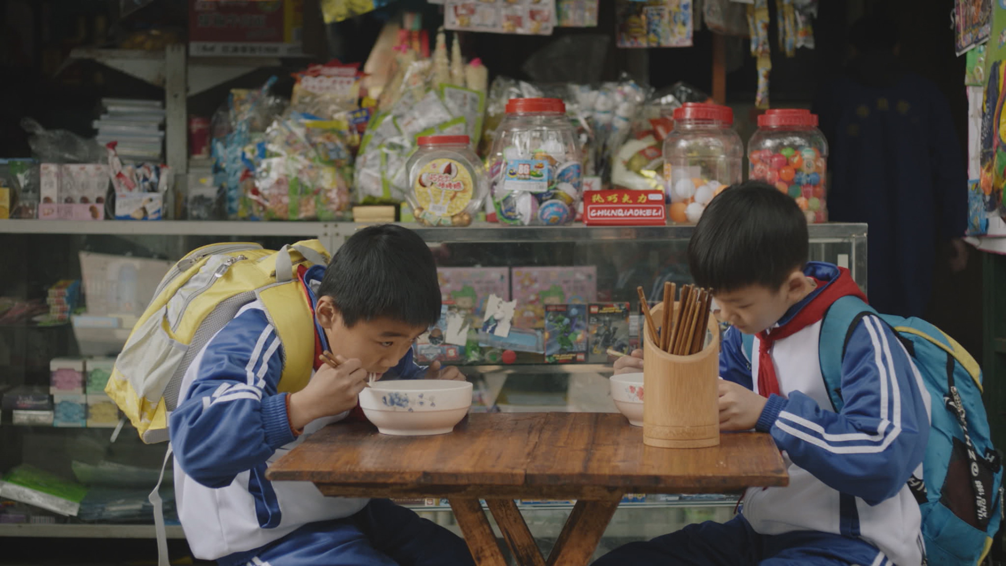 Two young boys sit at a table eating.