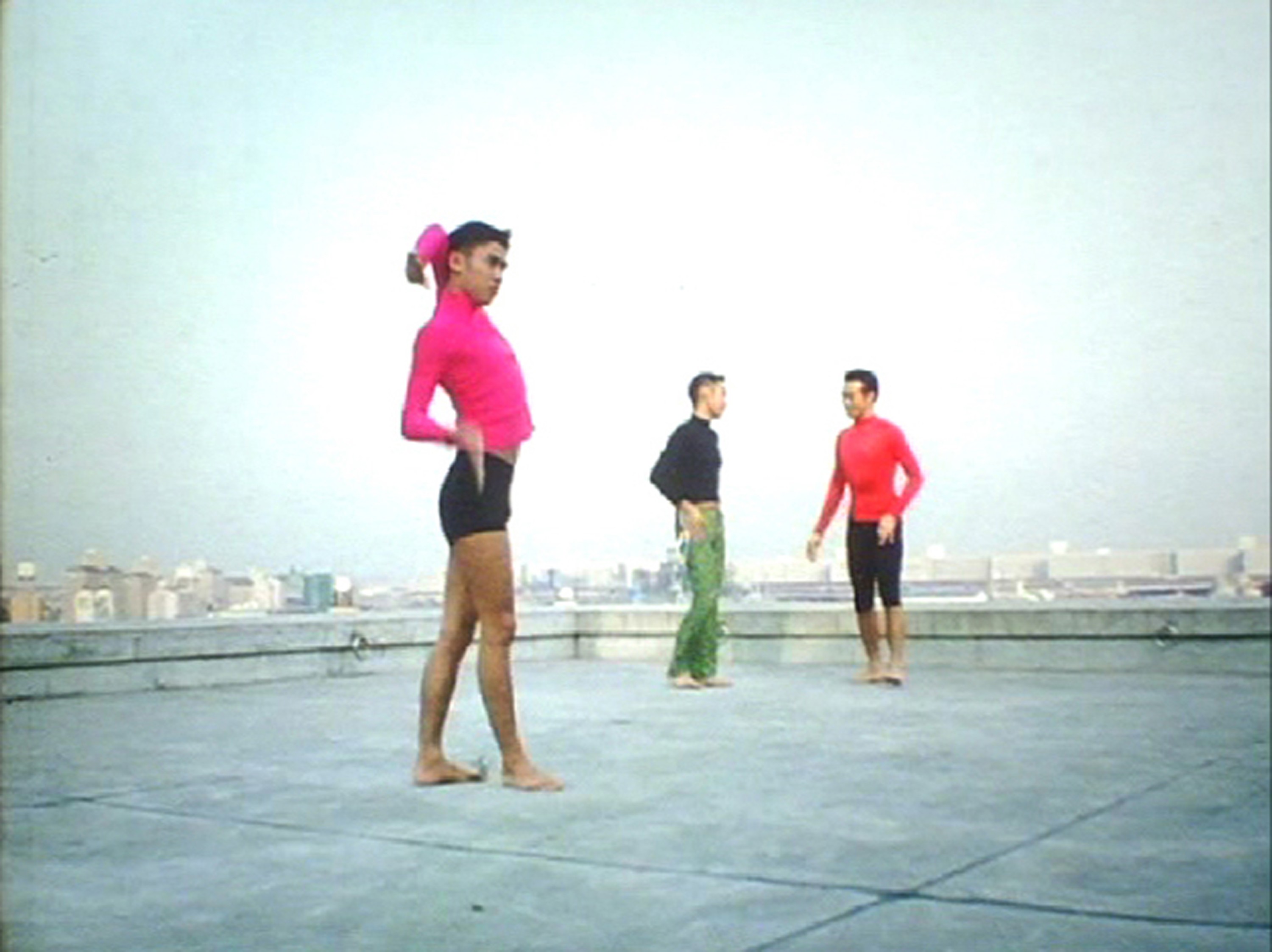 Three men in colourful outfits pose on a rooftop.