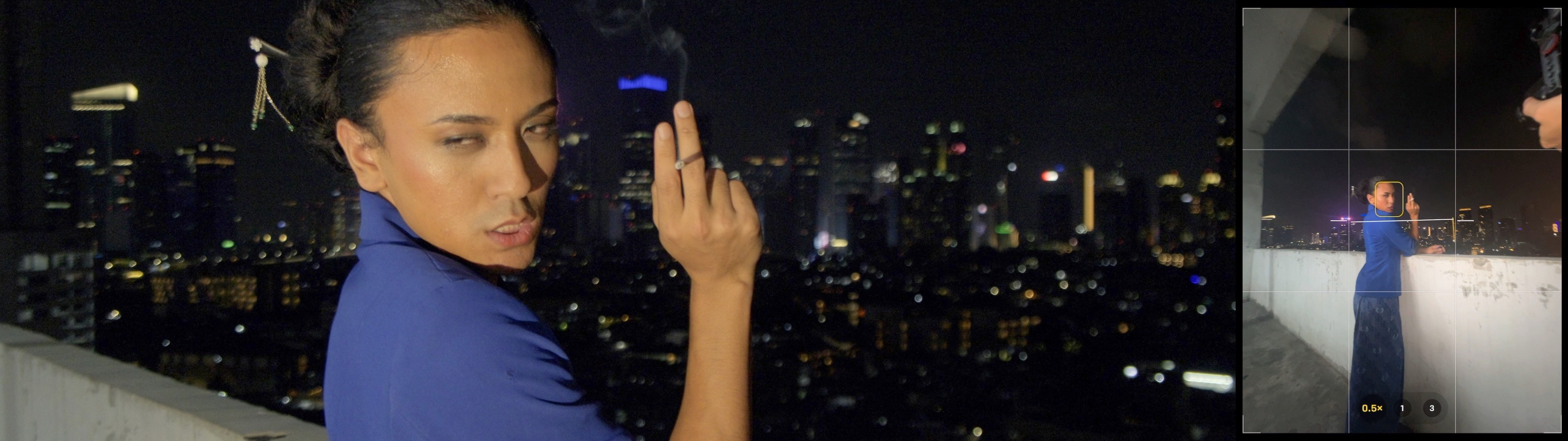 A performer in blue posing on a rooftop at night, with a city skyline behind them and an inset smartphone view of the same scene.