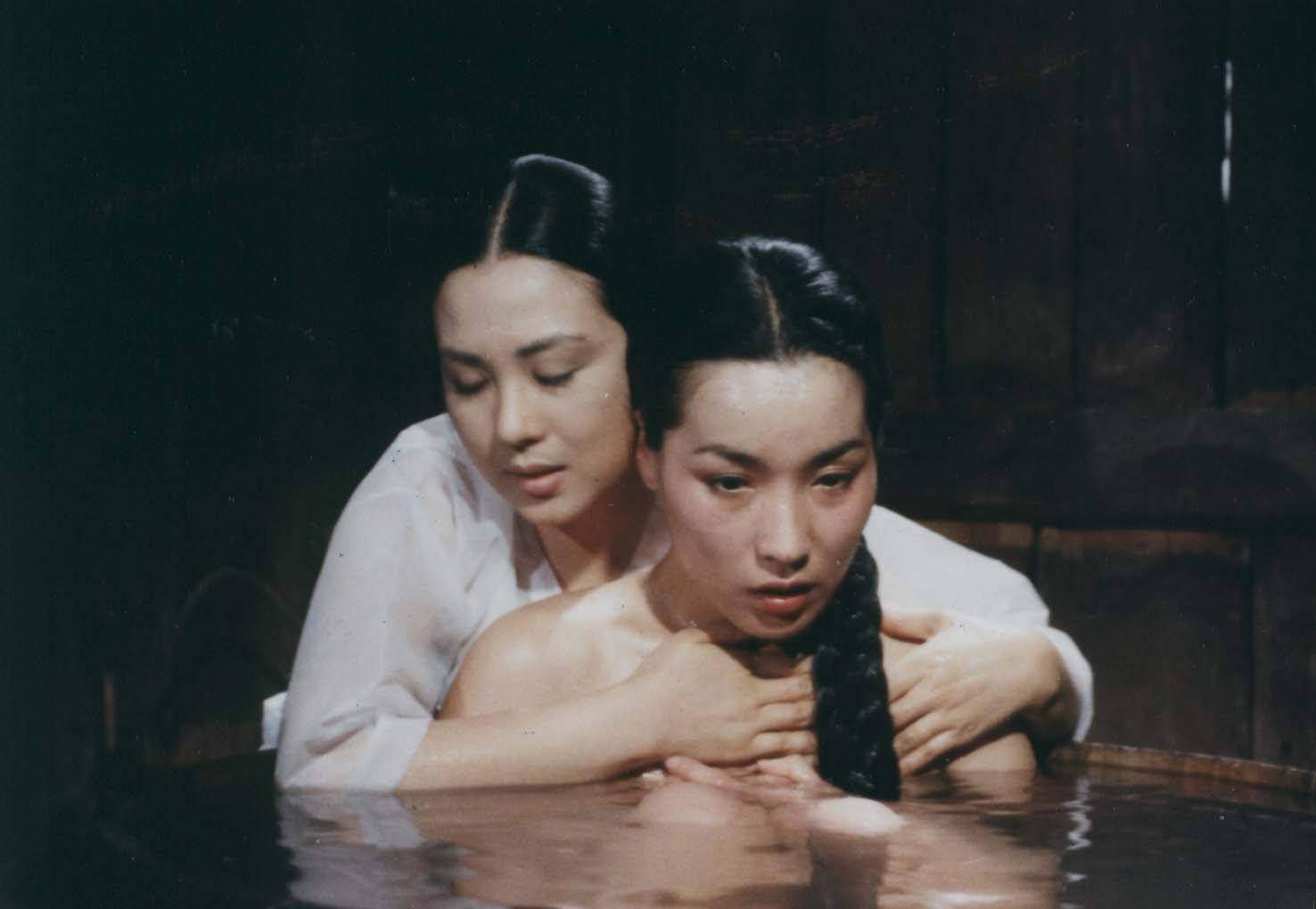 Two women embracing closely in a bath, one holding the other from behind.