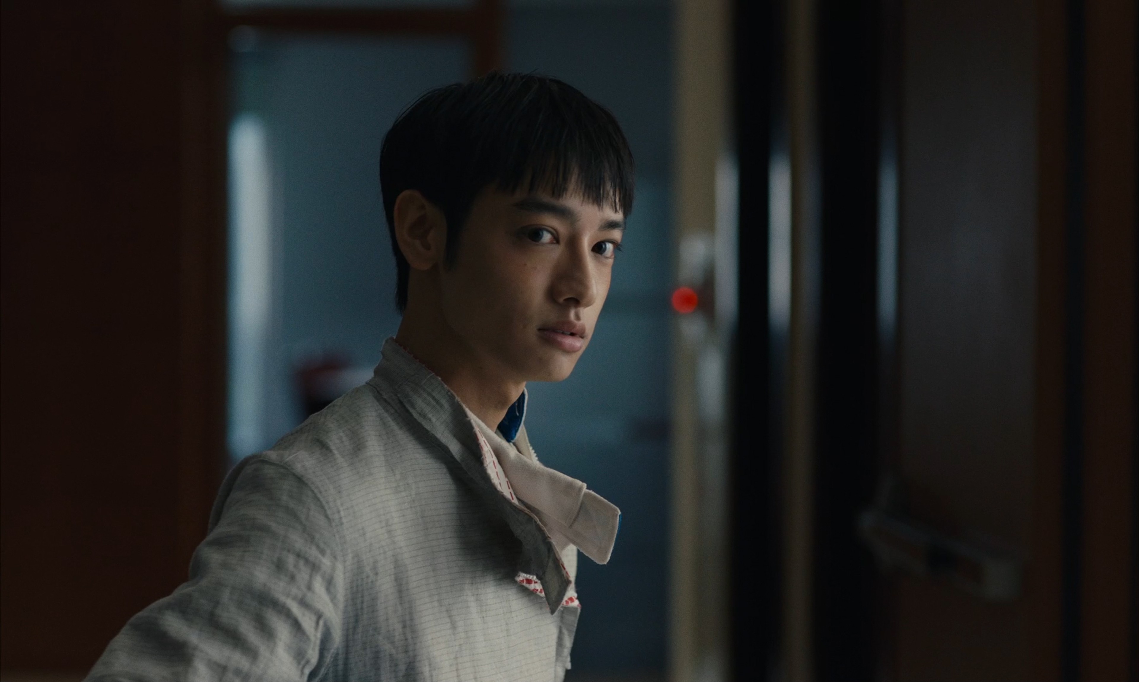 A young person standing in a dimly lit interior, looking back over their shoulder.