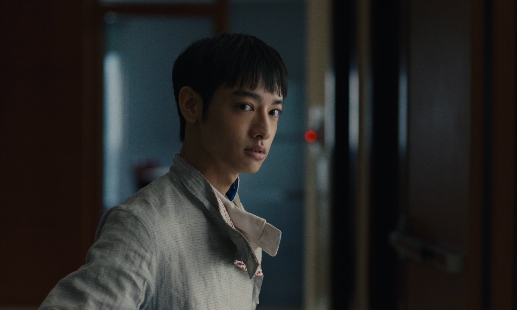 A young person standing in a dimly lit interior, looking back over their shoulder.