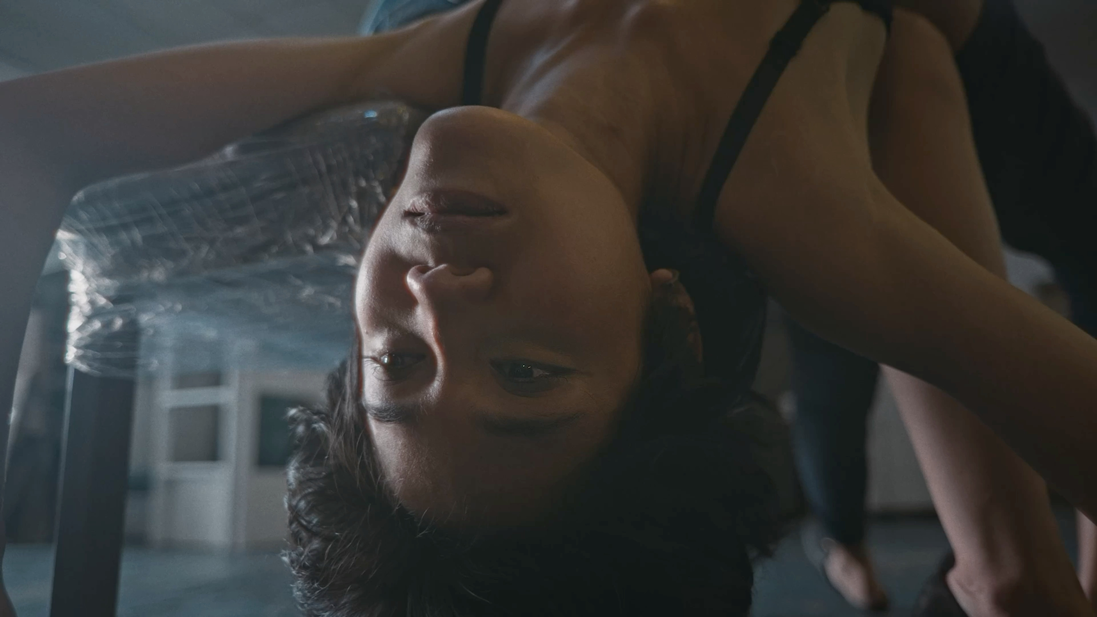 A person bending backwards over a chair, their face upside down in a dimly lit interior.