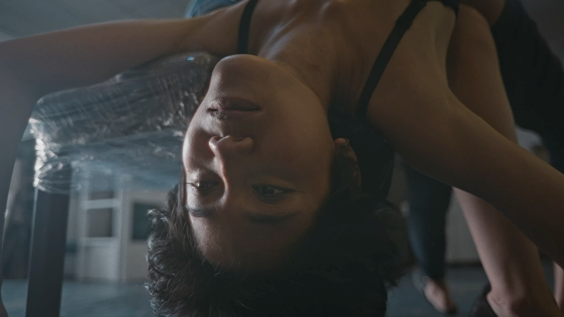 A person bending backwards over a chair, their face upside down in a dimly lit interior.