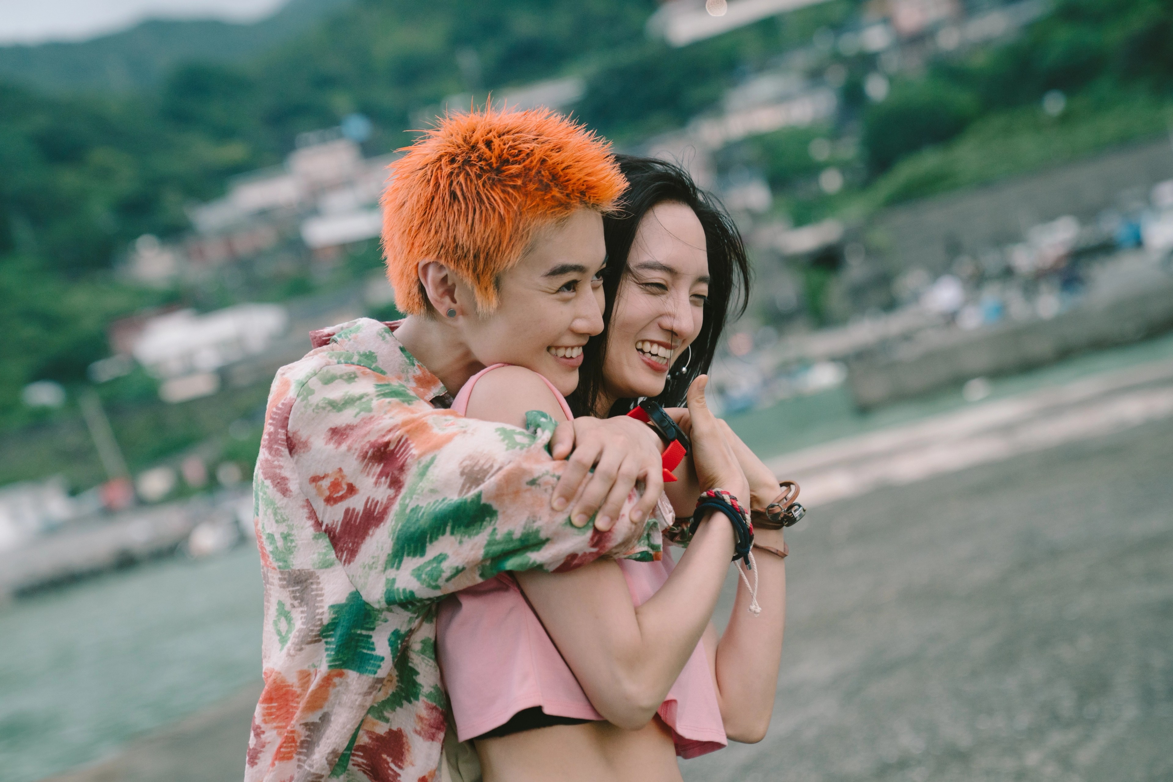 Two people smiling and embracing on a beach, with green hills in the background.