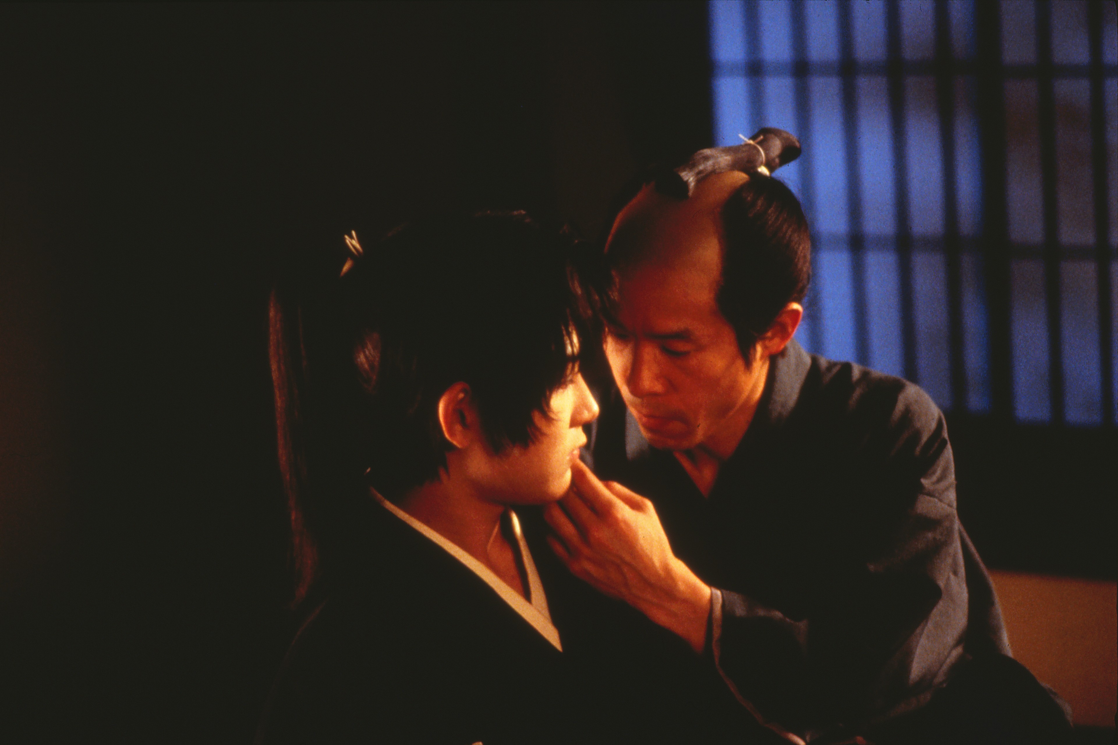 An older man touches the cheek of a younger man.