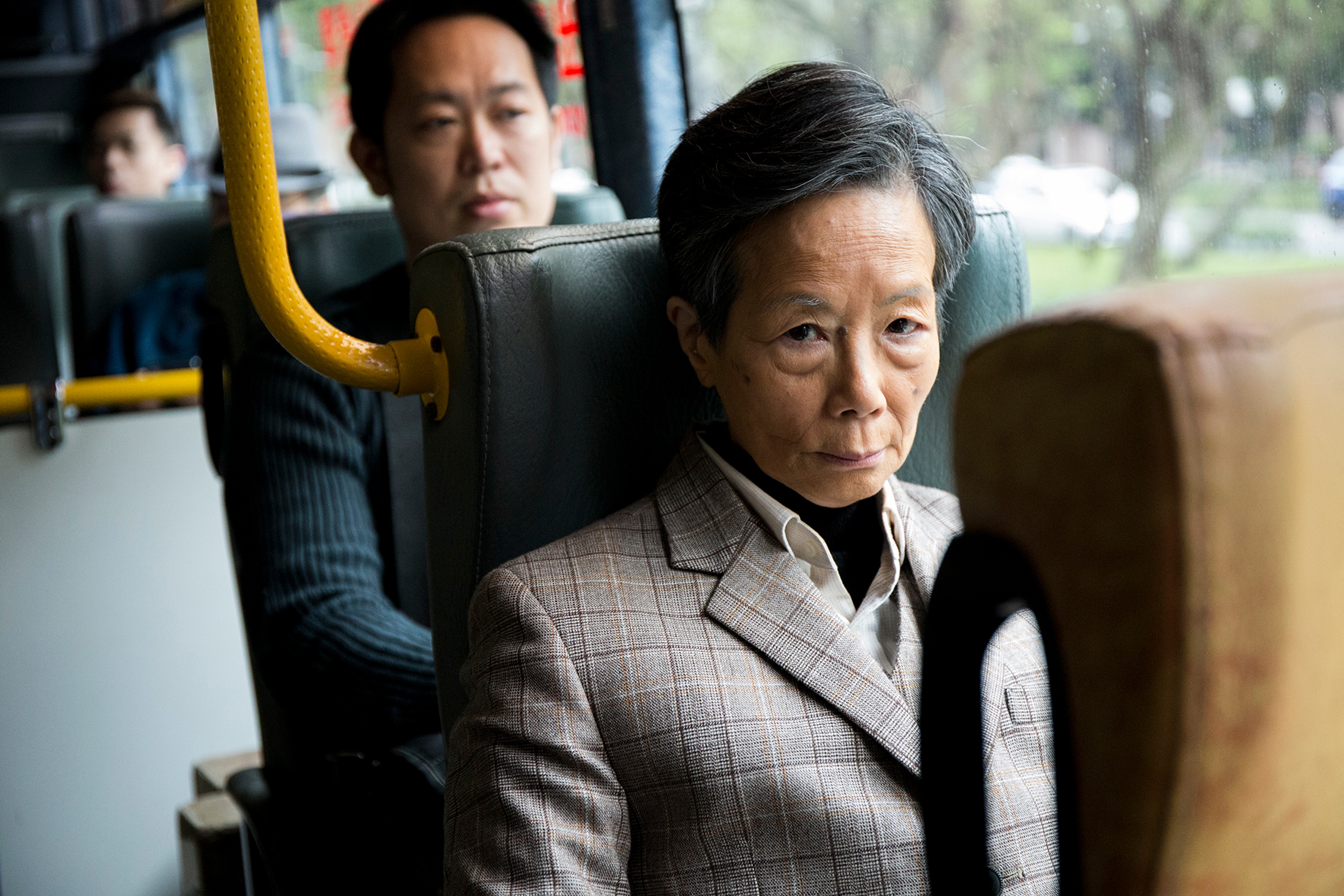 A person in a grey suit sitting on a bus.