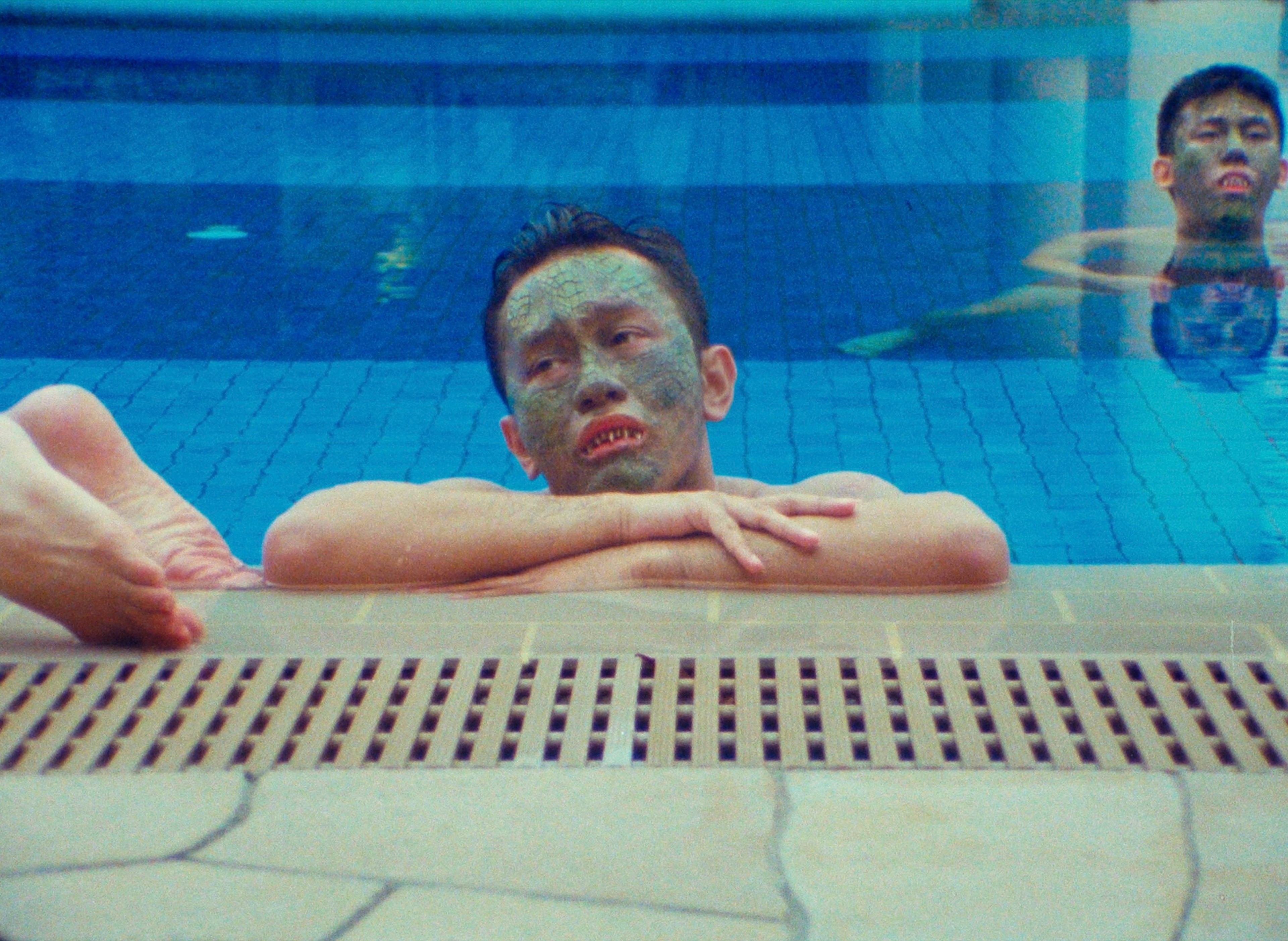 Two men with green scales on their face in a swimming pool.