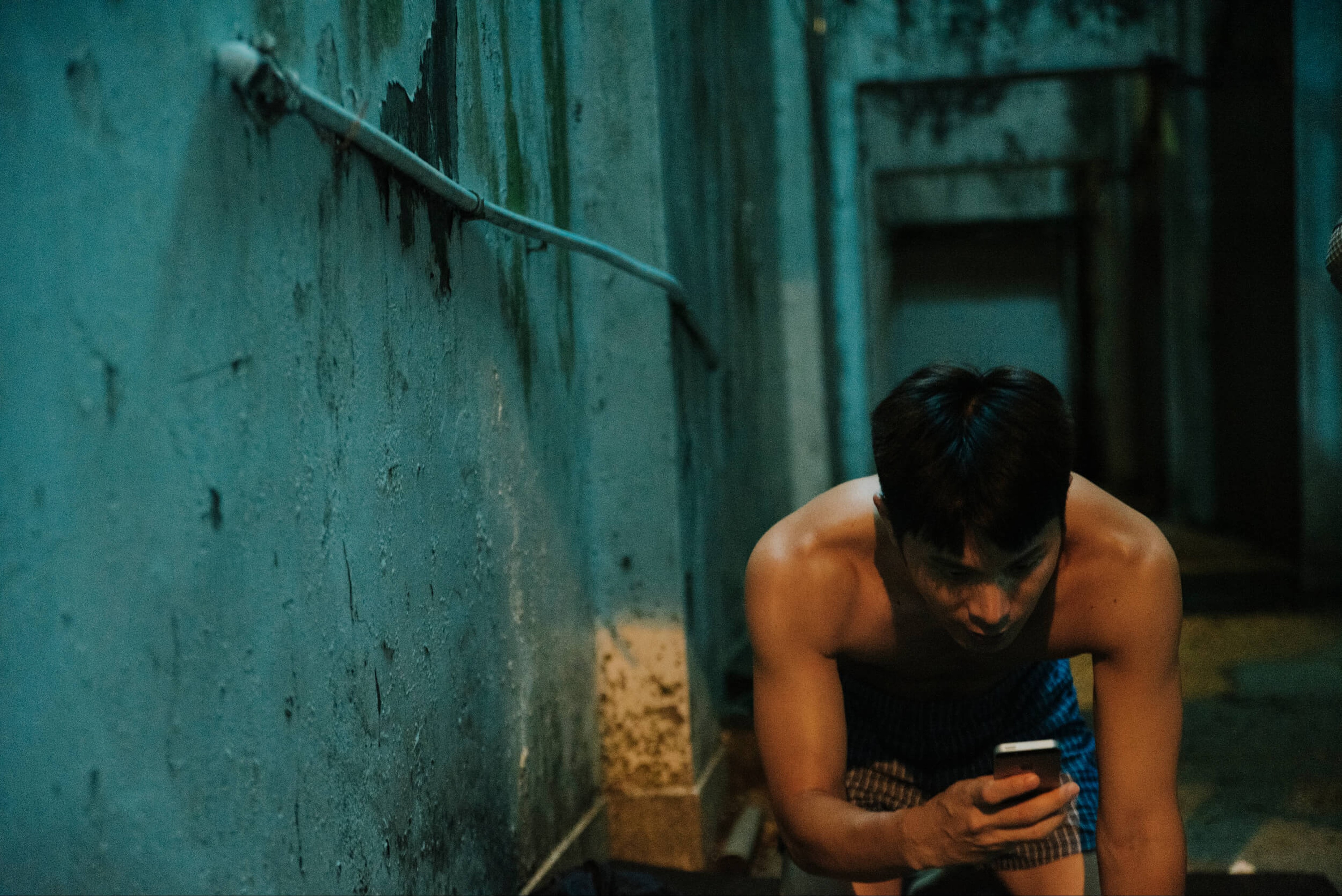 A crouching man looks at his phone.