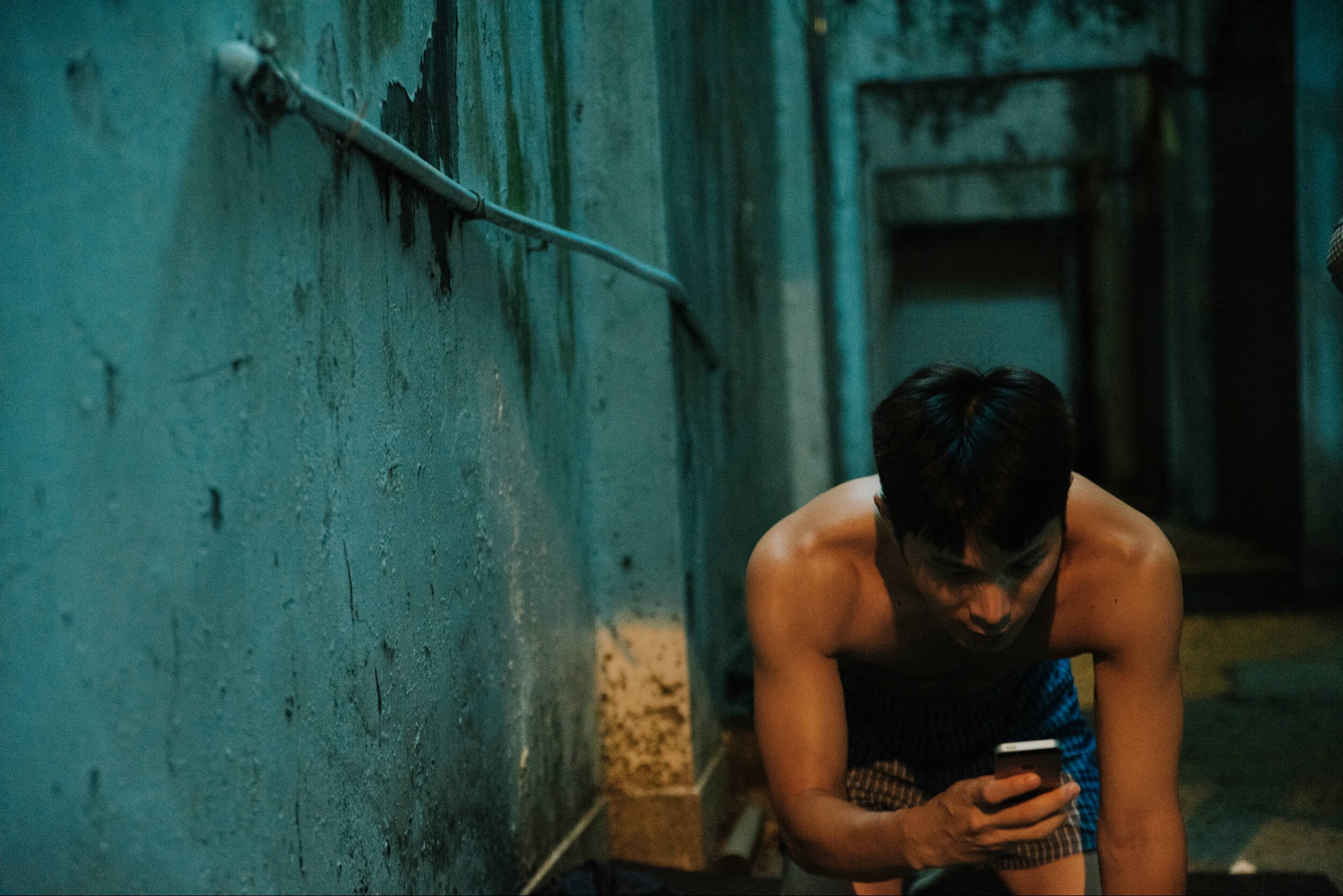 A crouching man looks at his phone.