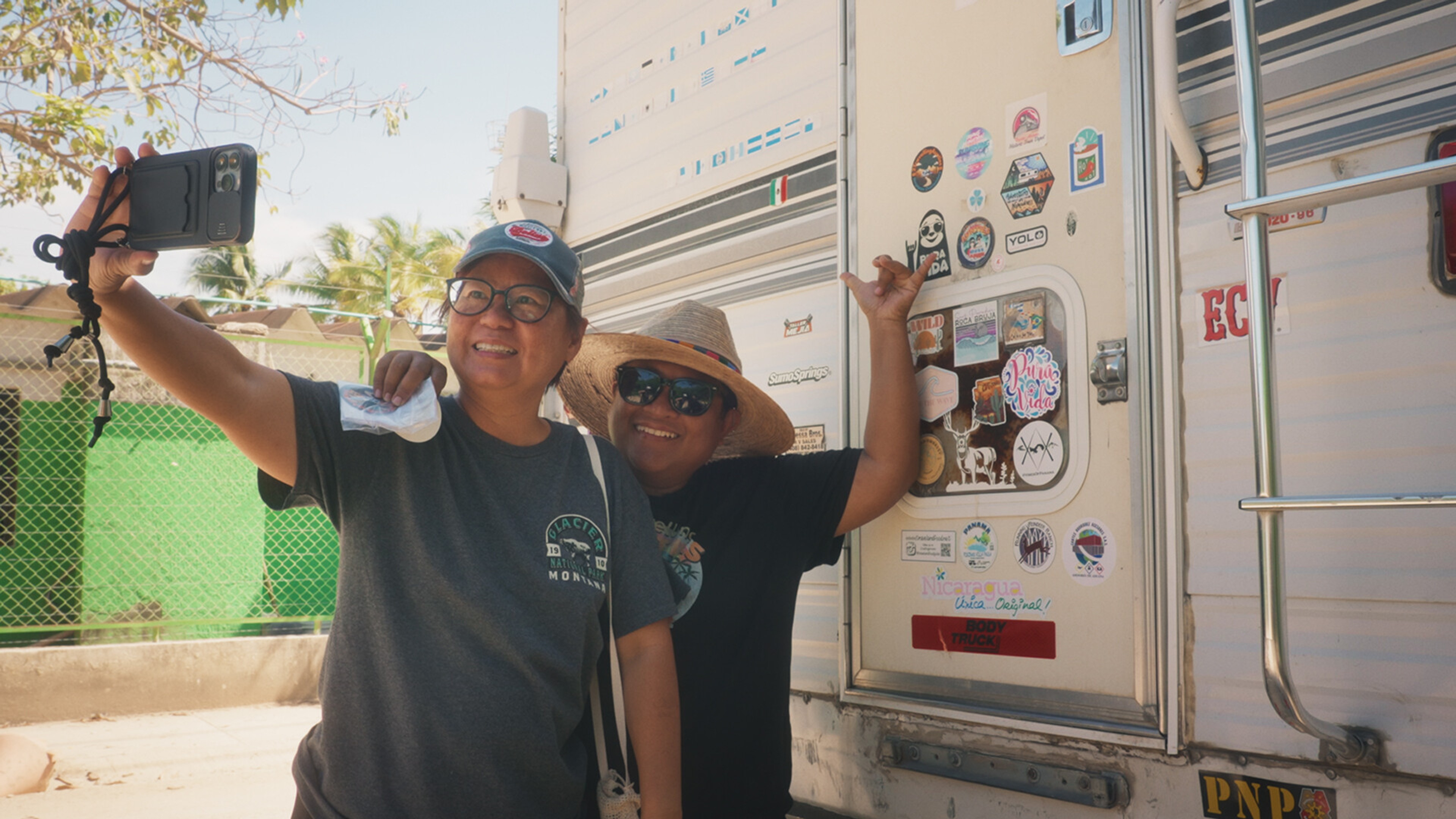 two middle-aged women take a selfie in front of a caravan.