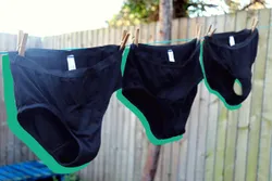 Three black Modibodi period pants hanging on washing line, with green outline