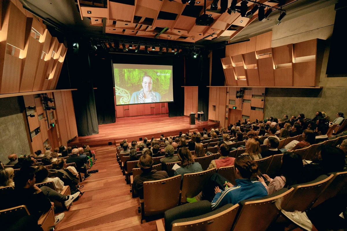 An warm event centre with seated attendees engaged in a speaker on stage.