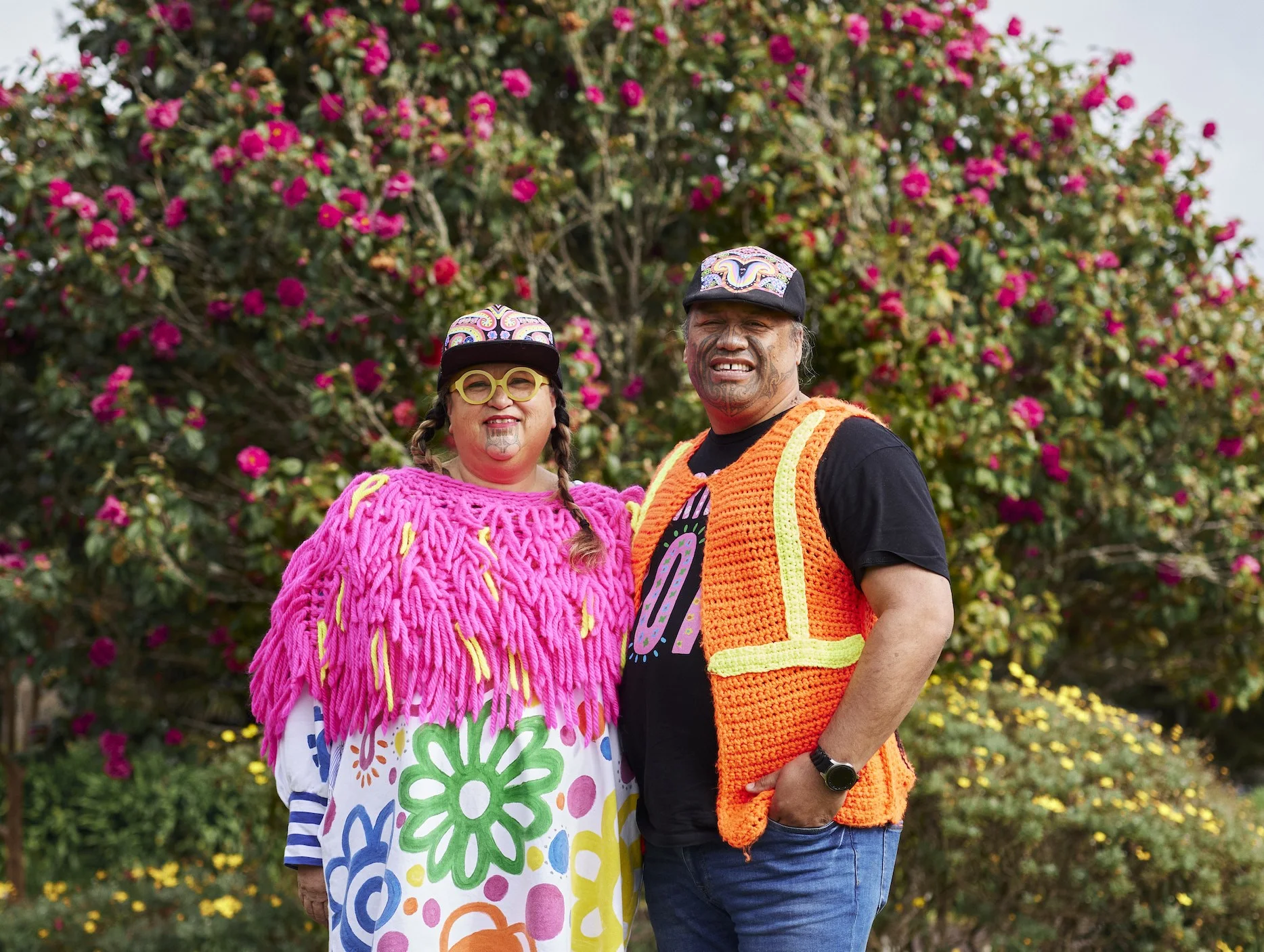 Lissy and Rudi wear neon clothes and stand in front of a flowering tree