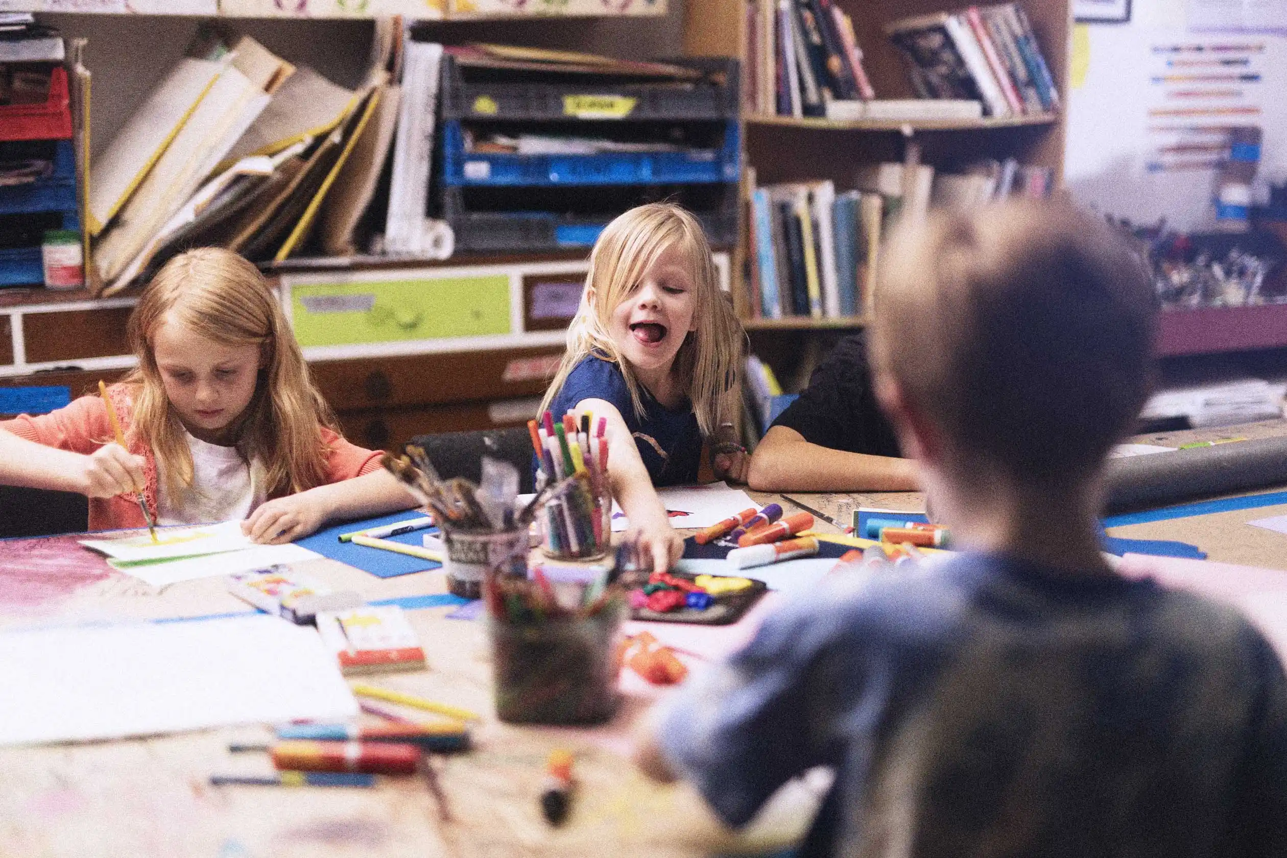 Four young children happily painting together around a table in art class, surrounded by paper, brushes and pens.