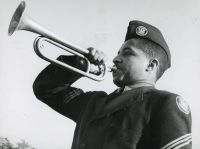 A Civilian Conservation Corps enrollee in dress uniform sounds a bugle, the CCC insignia on his cap — National Archives photo