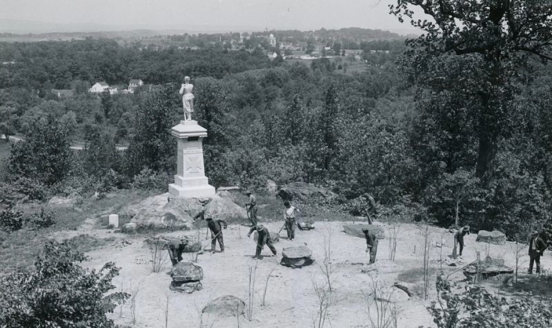 CCC laborers at work around a Civil War monument at Gettysburg, with the battlefield landscape beyond — historical photo