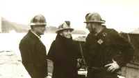 Frances Perkins, U.S. Secretary of Labor, in a hard hat speaking with two workers at a worksite