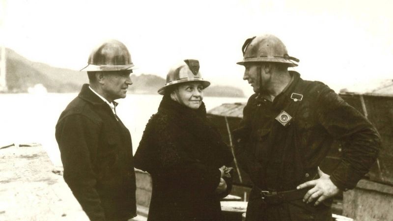 Frances Perkins, U.S. Secretary of Labor, in a hard hat speaking with two workers at a worksite