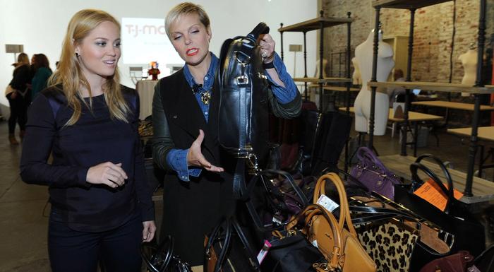 Jenn Rogien and Erika Christensen standing in front of a screen displaying the TJMaxx logo and holding up a purse