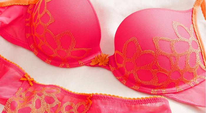 A close up photo of a bright pink bra and underwear set with orange lace details