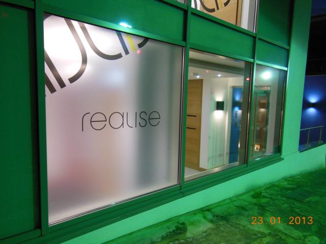 Night view through green-lit glass doors into the Realise reception, with frosted glass carrying the 'realise' logo
