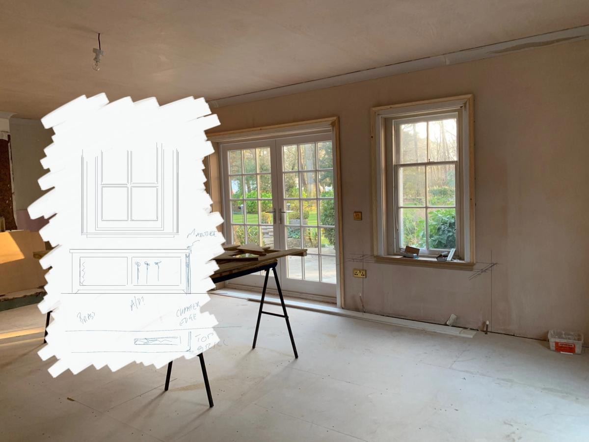 Photo of an empty room under renovation with French windows, with a white-painted patch on the far wall carrying a pencil sketch of panelled joinery