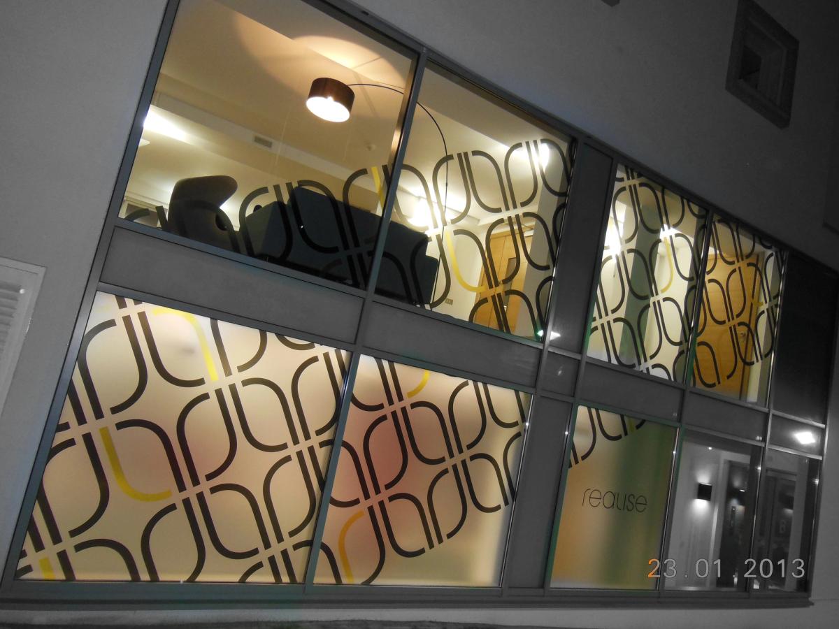 Office windows at night lit from inside, with a large interlocking-loop frosted pattern across the glazing