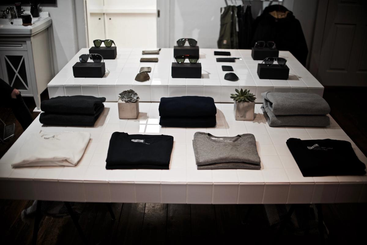 White display tables arranged with folded knitwear, sunglasses and small plants in a bright shop interior