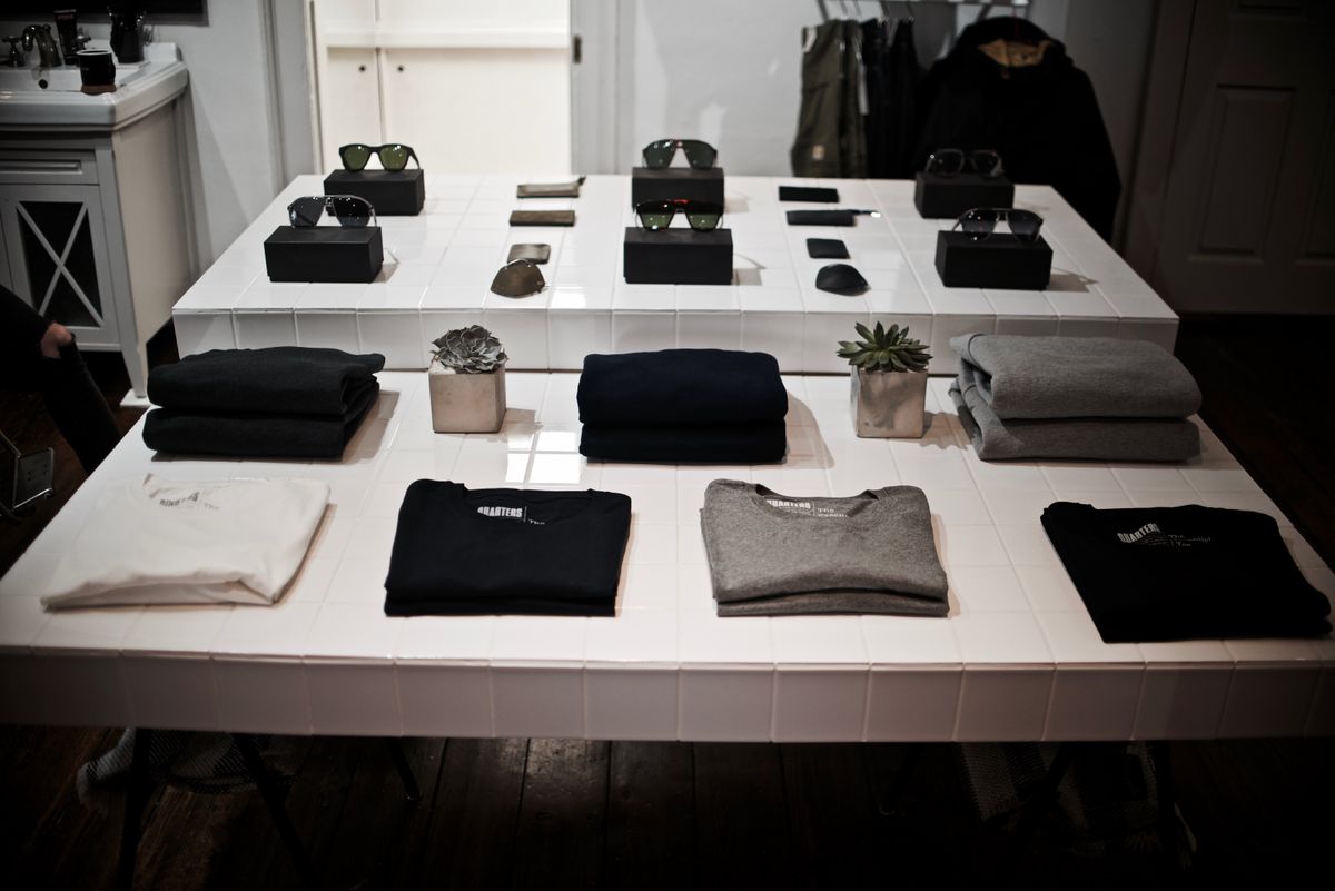White display tables arranged with folded knitwear, sunglasses and small plants in a bright shop interior