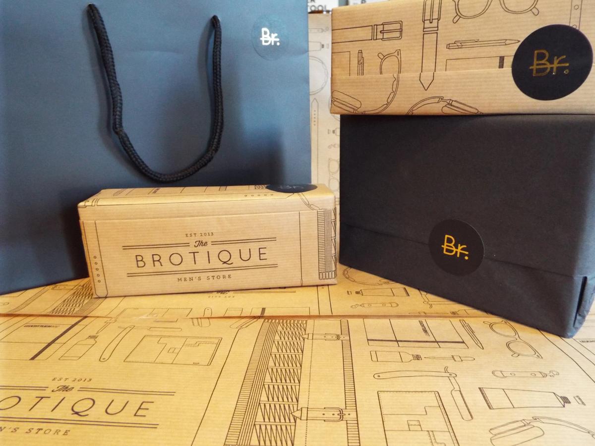 Brotique packaging: a navy carrier bag, a printed kraft box and a navy-wrapped box with a round 'Br.' sticker, on the illustrated wrapping paper