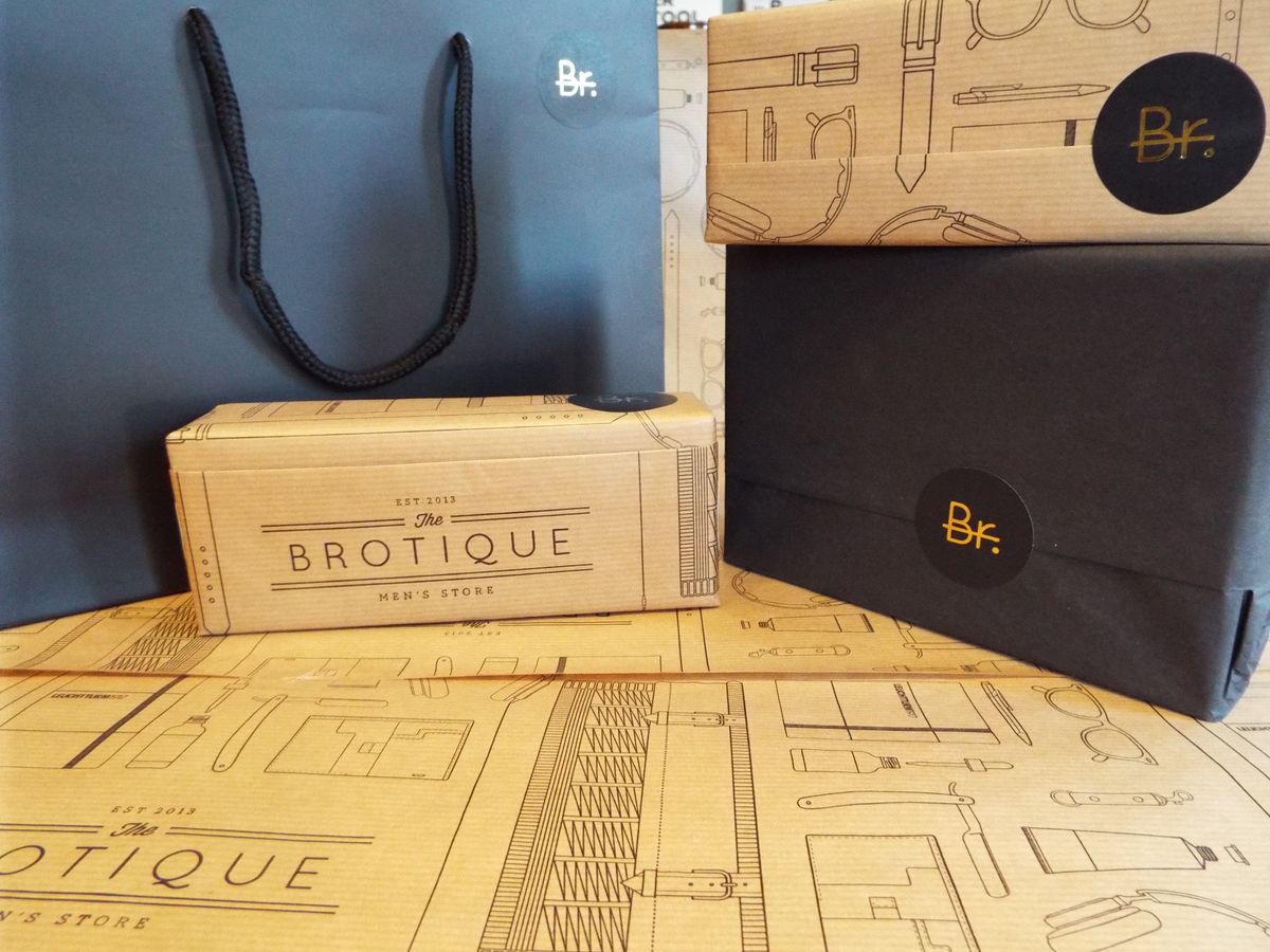 Brotique packaging: a navy carrier bag, a printed kraft box and a navy-wrapped box with a round 'Br.' sticker, on the illustrated wrapping paper
