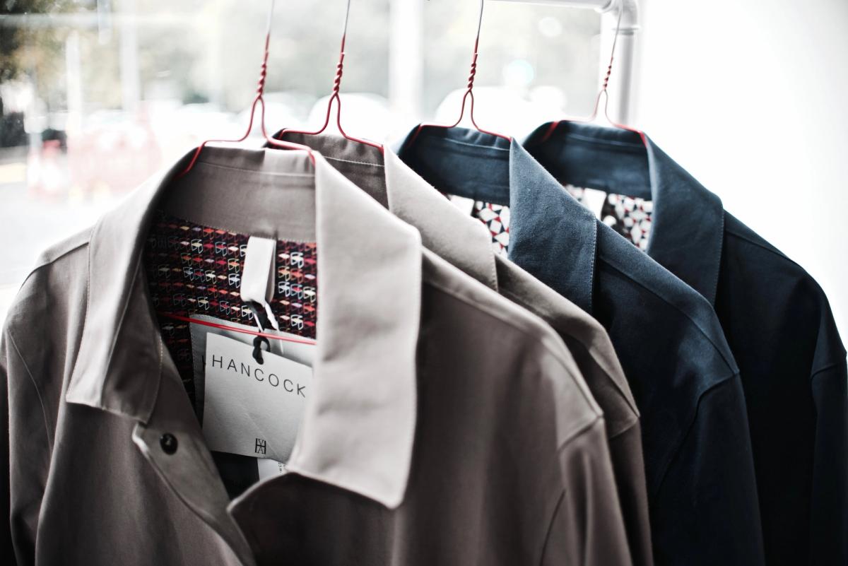 Jackets in grey, navy and black hanging on a rail, one showing a 'Hancock' label inside the collar