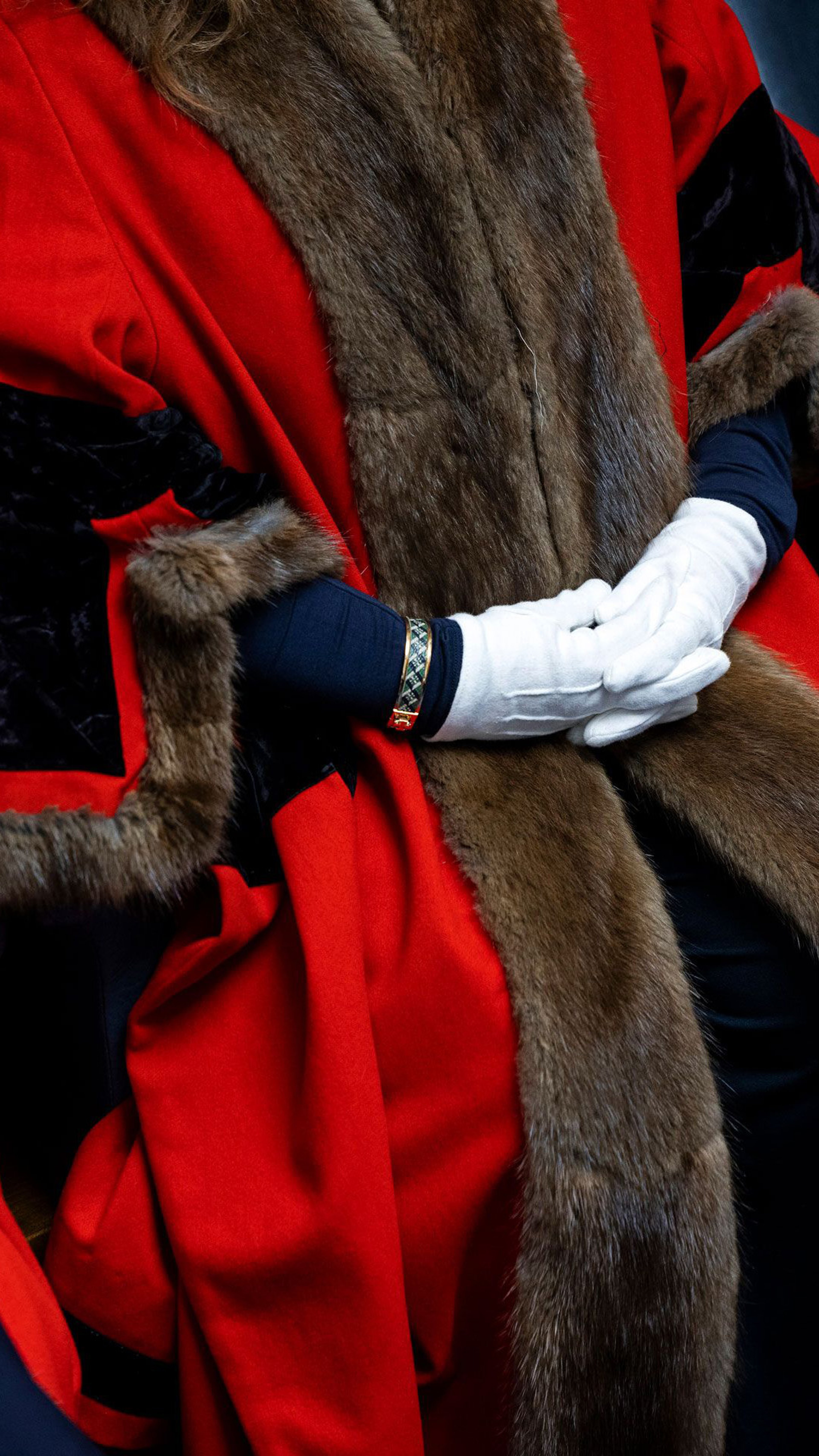 Close up of a persons hands. They are wearing white and a red robe