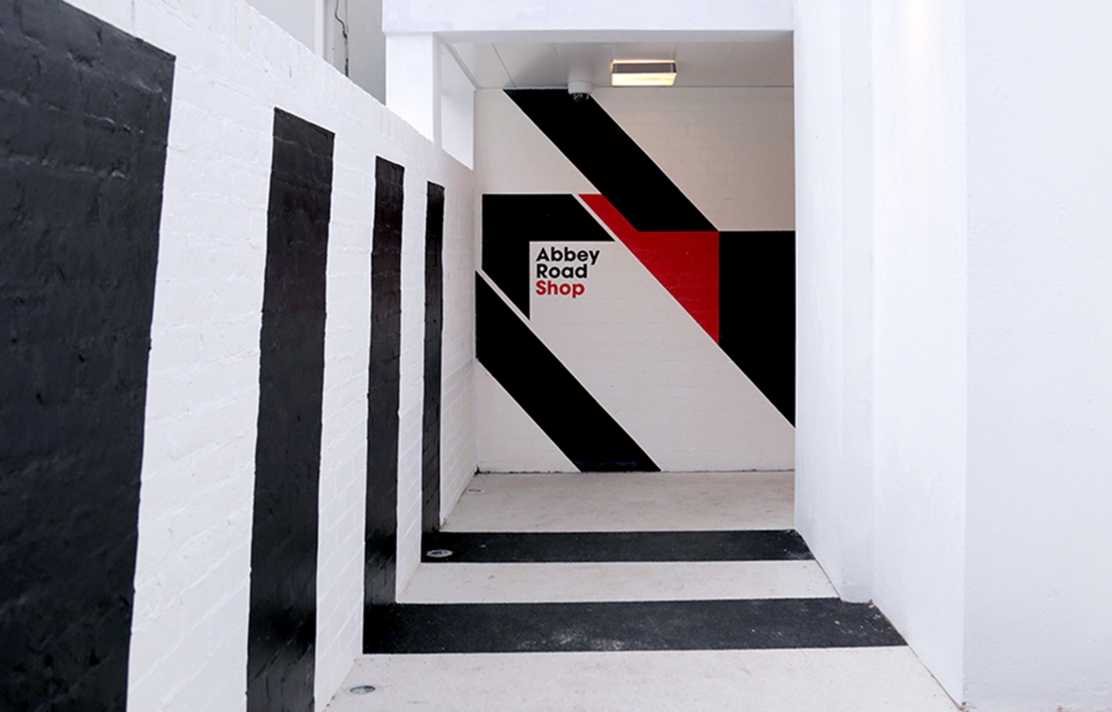 Photograph showing interior corridor branding of Abbey Road studios shop. White walls with black stripes.