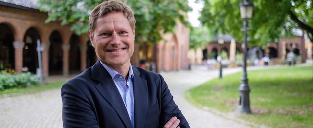 Mann i dressjakke som smiler til kamera.